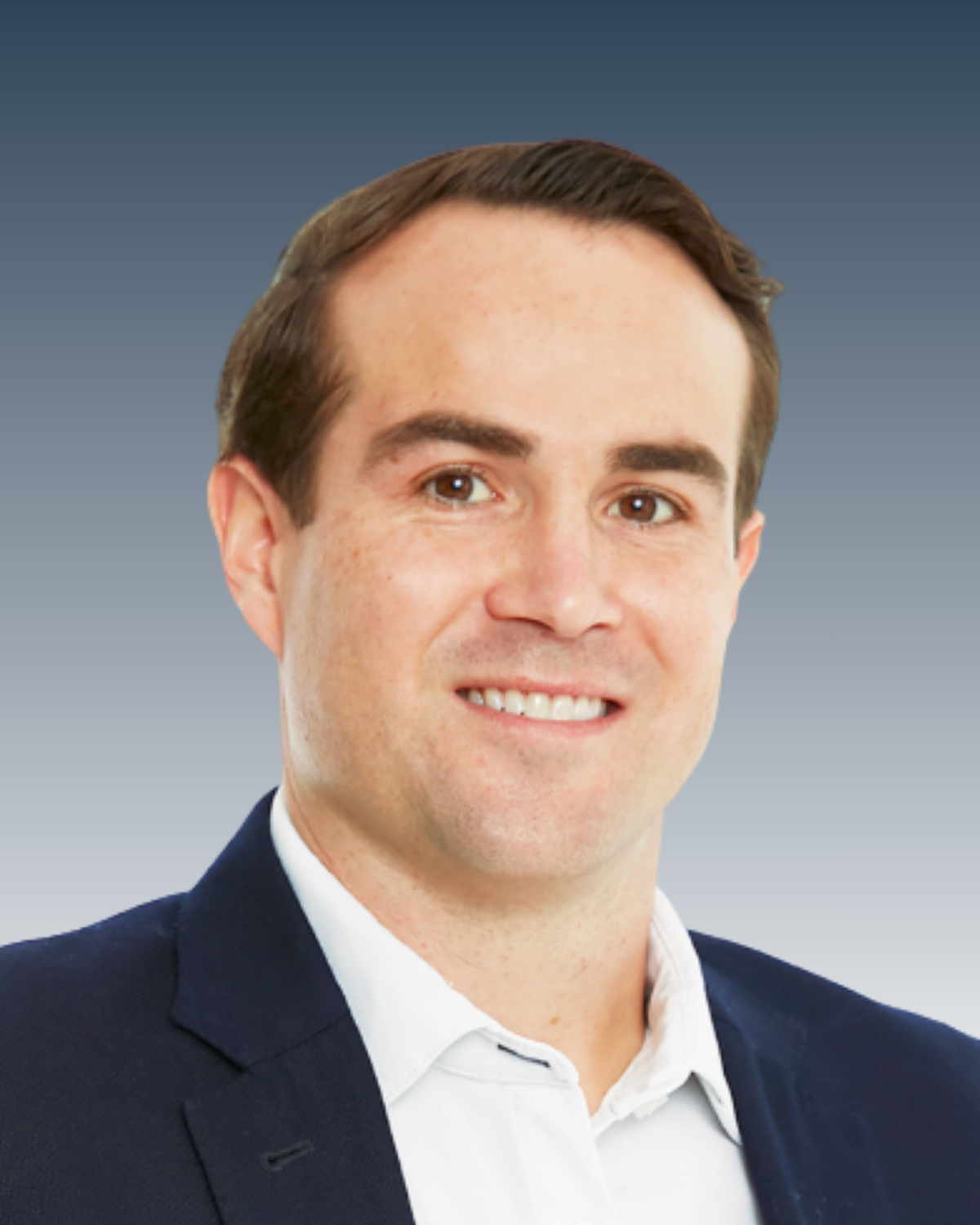 A professional headshot of a man with short brown hair, wearing a dark suit jacket and white shirt, smiling in front of a gradient blue background.