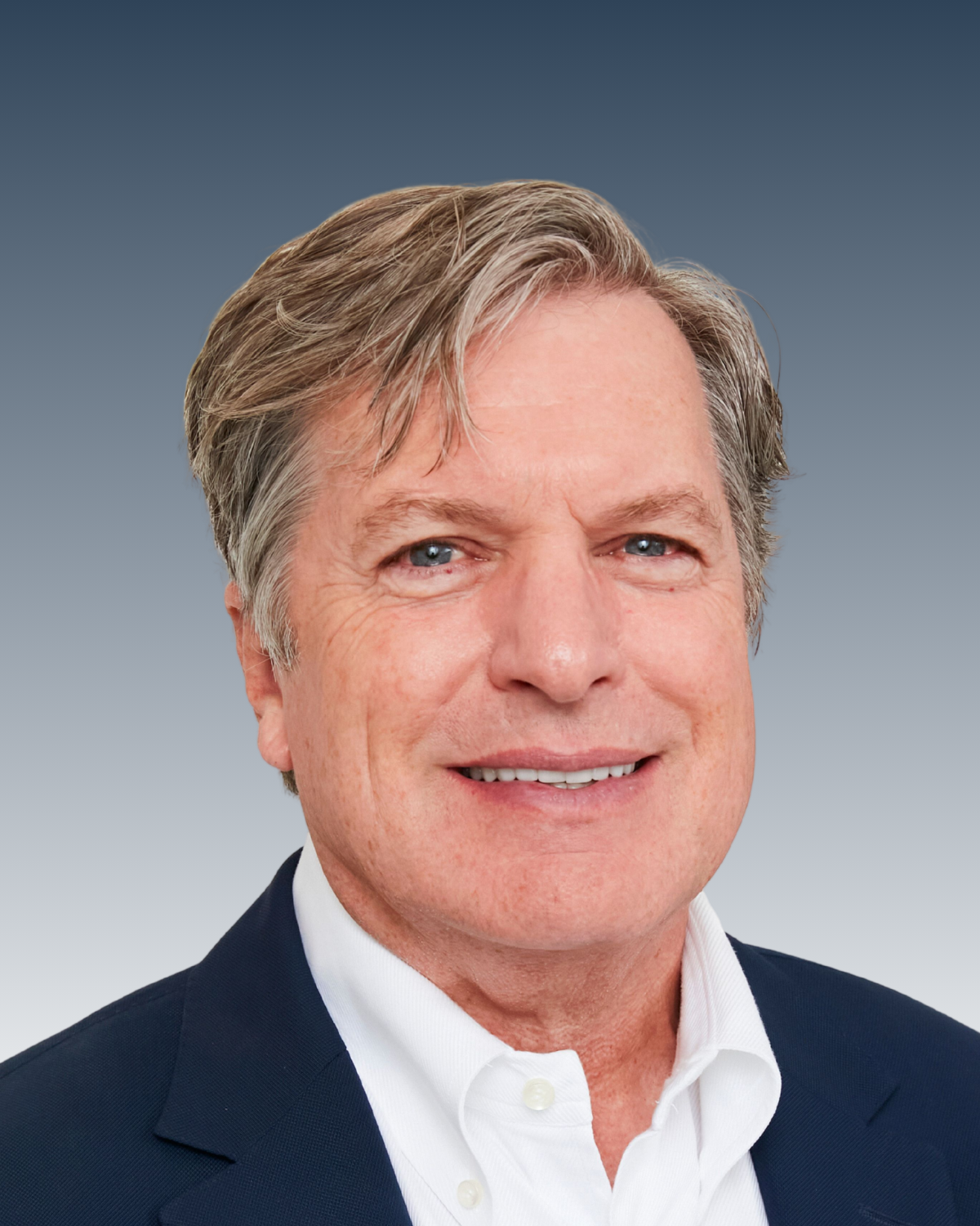 Headshot of a middle-aged man with gray hair, smiling, wearing a dark suit jacket and a white collared shirt against a blue gradient background.