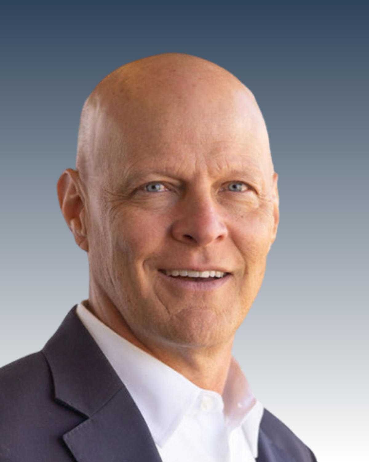 Close-up image of a middle-aged man with a bald head, blue eyes, and a friendly smile, dressed in a dark suit and white shirt, against a gradient background.