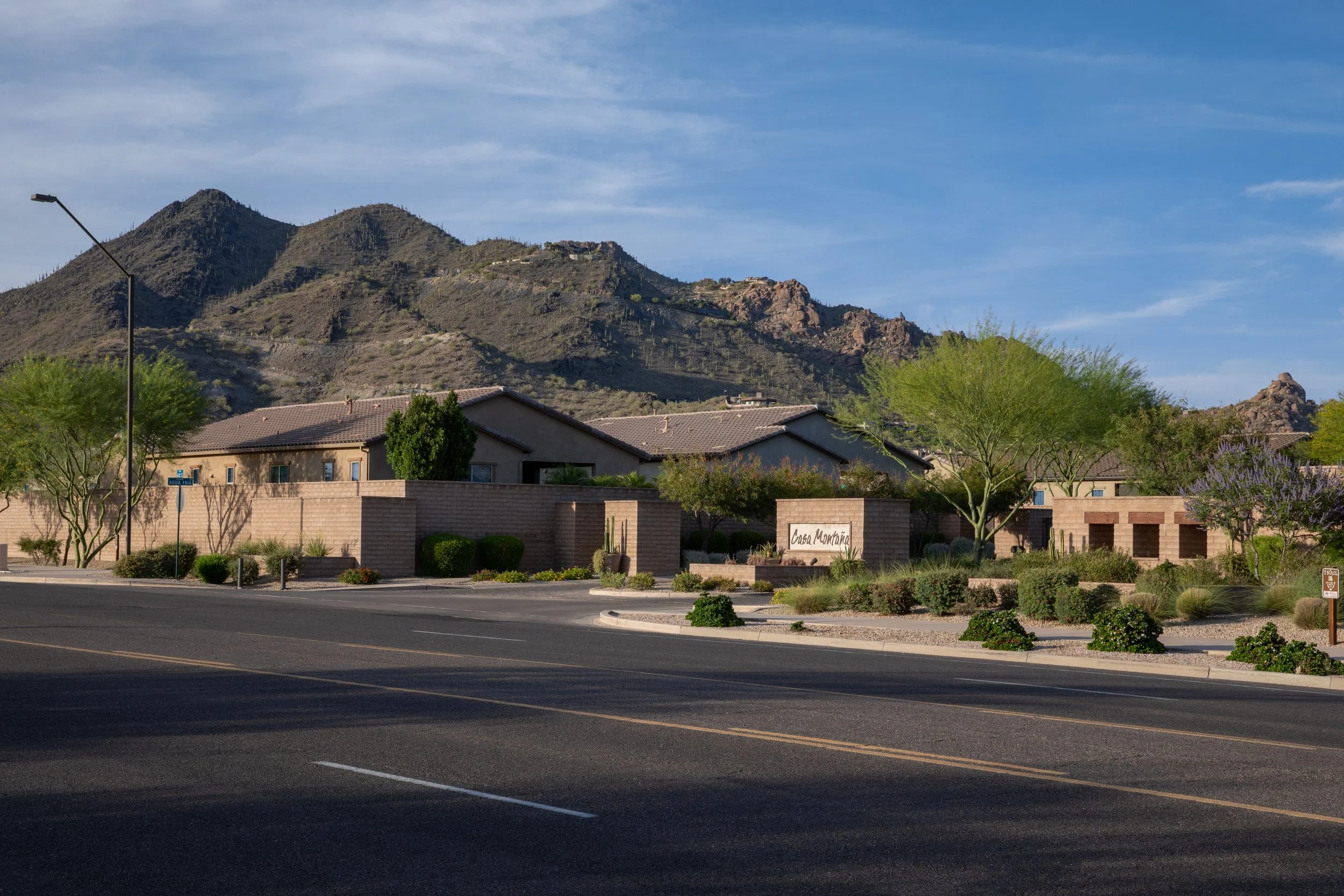 Residential neighborhood at the base of a mountain with desert vegetation, single-story houses, and a clear blue sky.