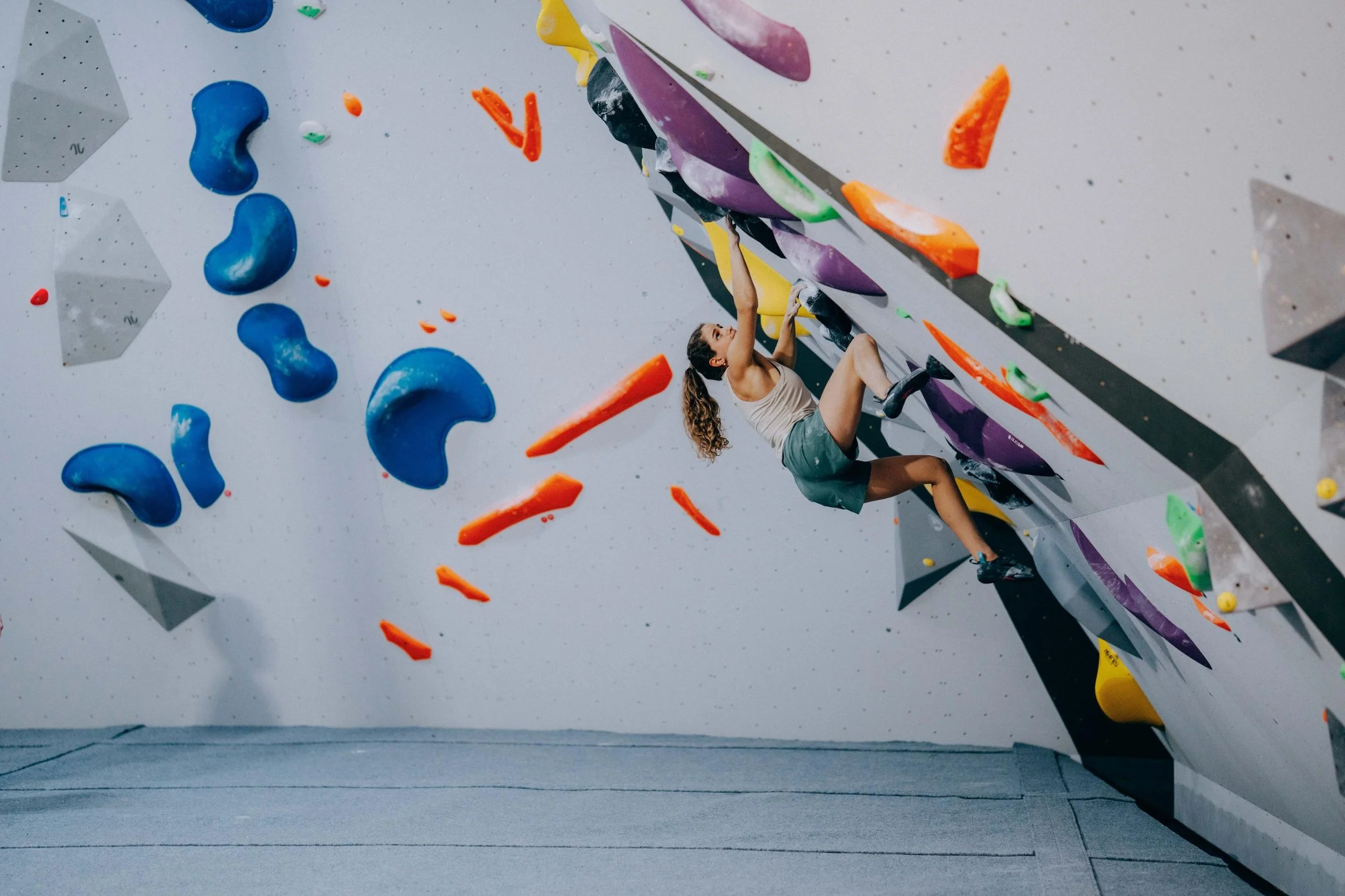 A woman climbing a colorful indoor rock climbing wall with various holds and grips.