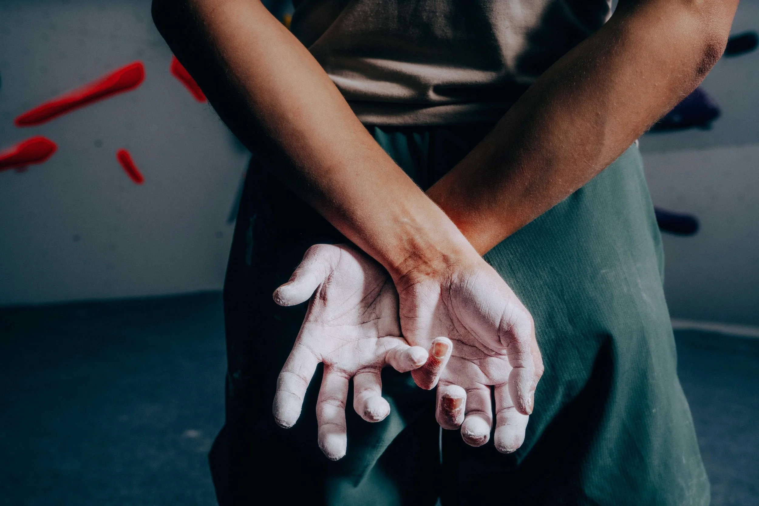 Person with chalk dust on hands helping another person. Focus on arms and hands, drills or climbing gear in the background.