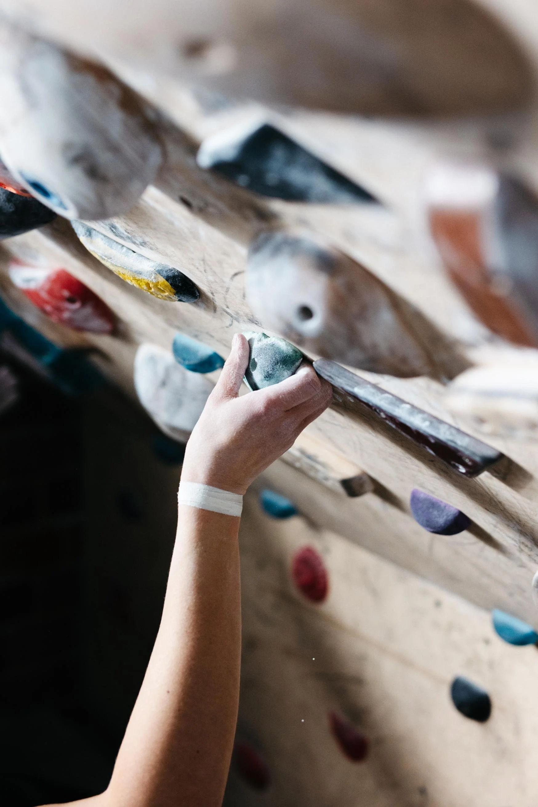 A person’s arm and hand reaching for a rock climbing hold on an indoor climbing wall with colorful holds.