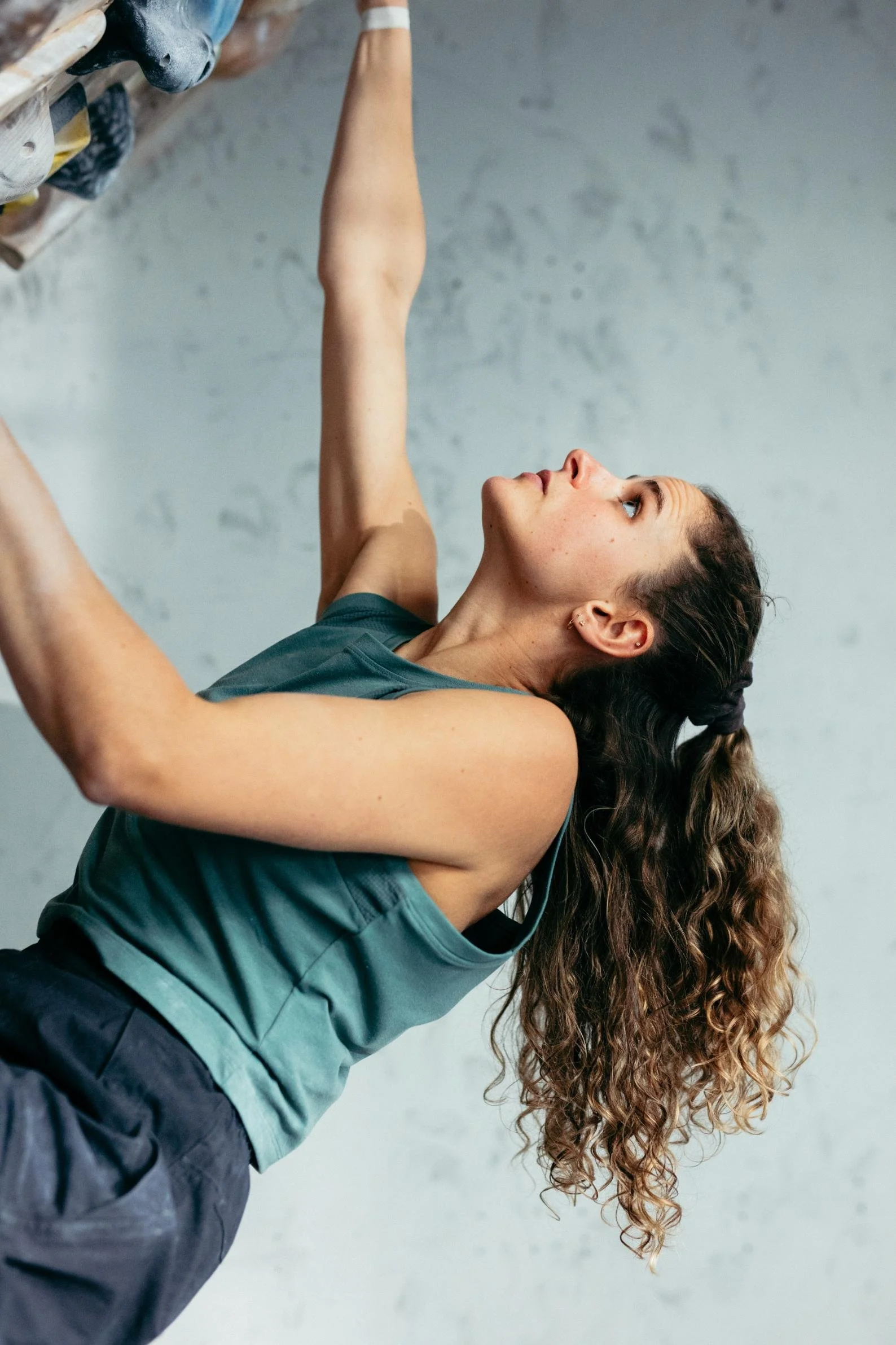 A woman with long curly hair performing a hanging exercise indoors, wearing workout clothes.