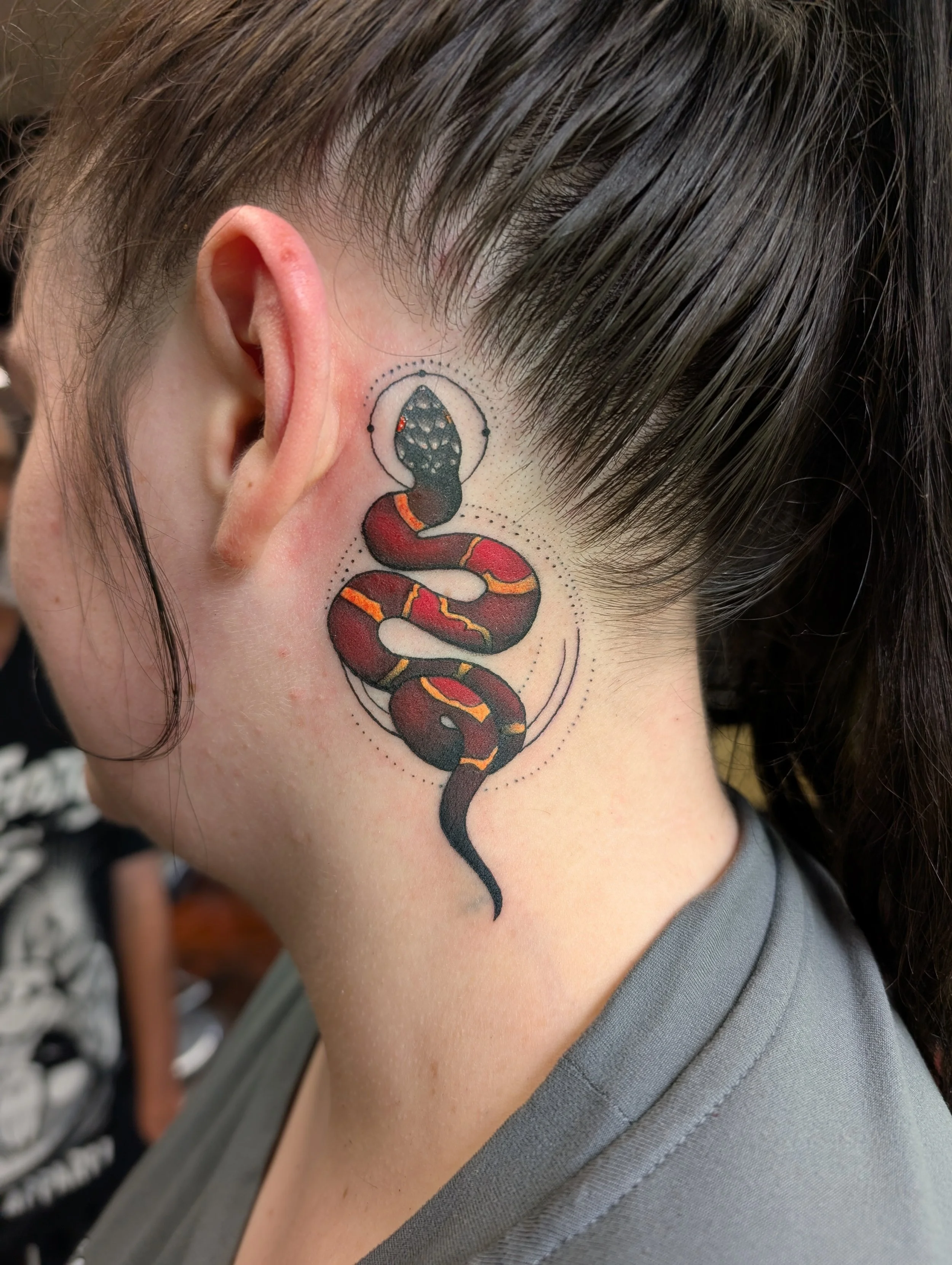 Close-up of a person's neck with a tattoo of a snake wrapped around an object, featuring vibrant colors and detailed shading.