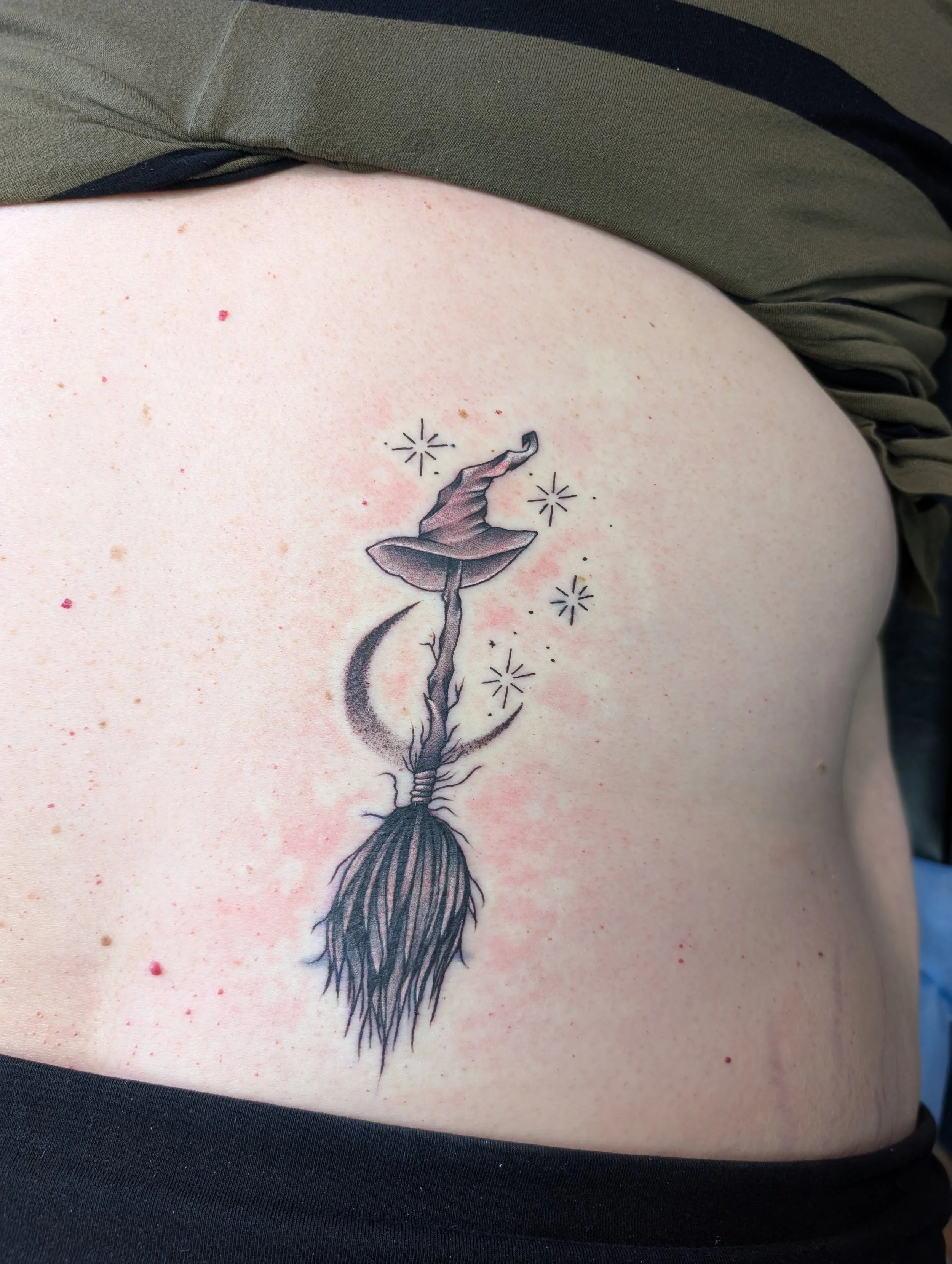 A tattoo of a whimsical flower with a moon-shaped stem, surrounded by small starbursts, on person's side.