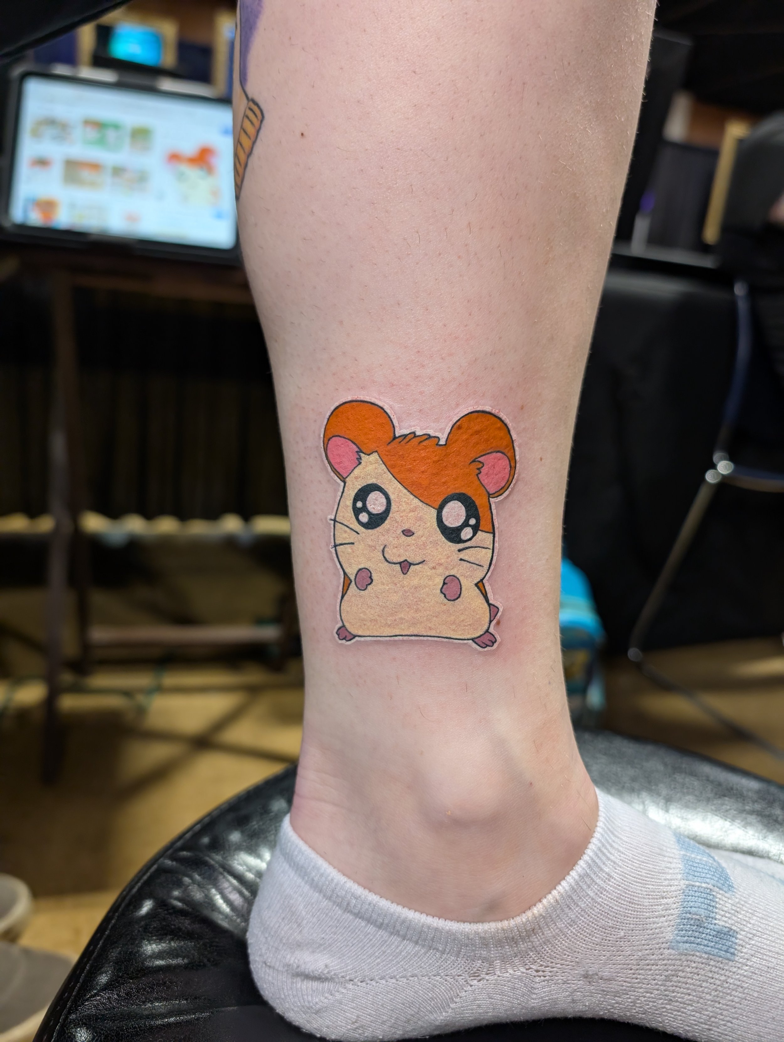 A person's lower leg with a cute hamster cartoon tattoo near the ankle.
