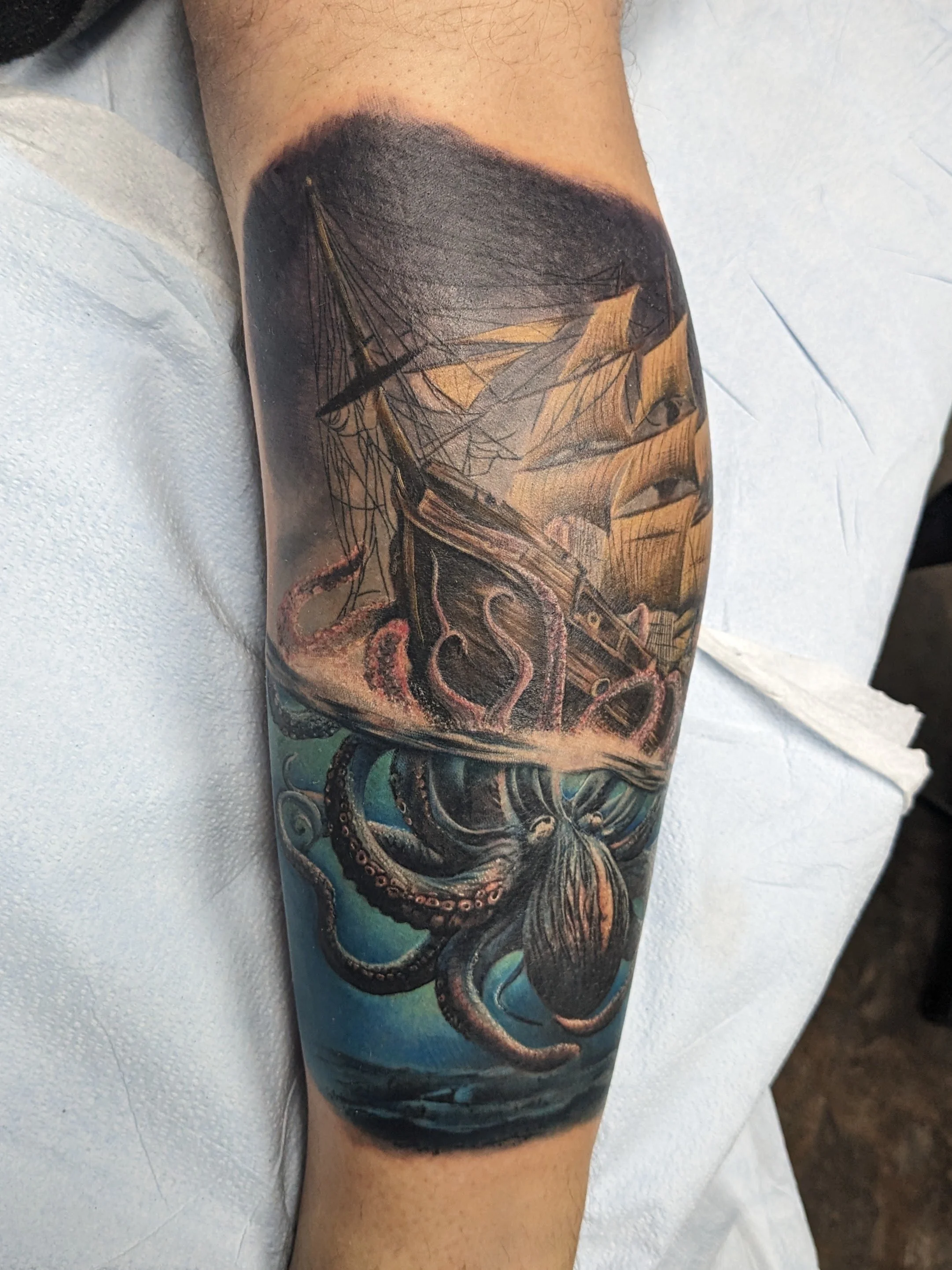 Colorful tattoo of a large octopus with swirling tentacles on a person's arm, with a background of black, blue, and orange hues.