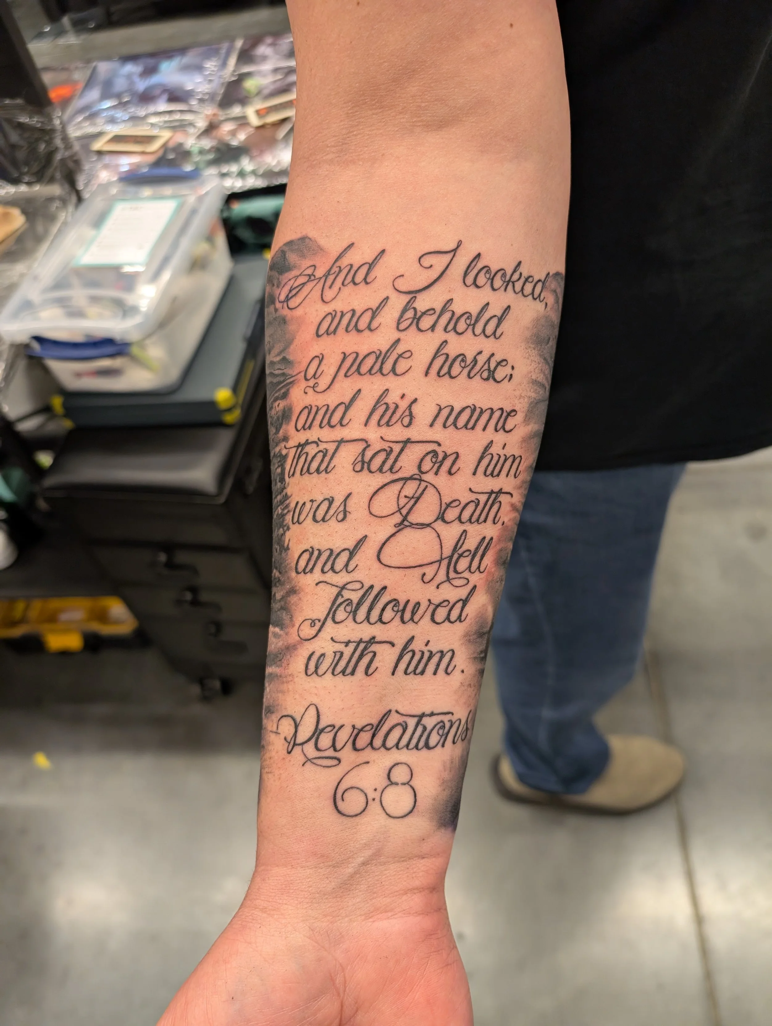Close-up of a person's forearm with a tattoo of a quote in elegant cursive script. The tattoo says, 'And I looked, and behold a pale horse: and his name that sat on him was Death, and Hell followed with him,' with a decorative flourish at the bottom.