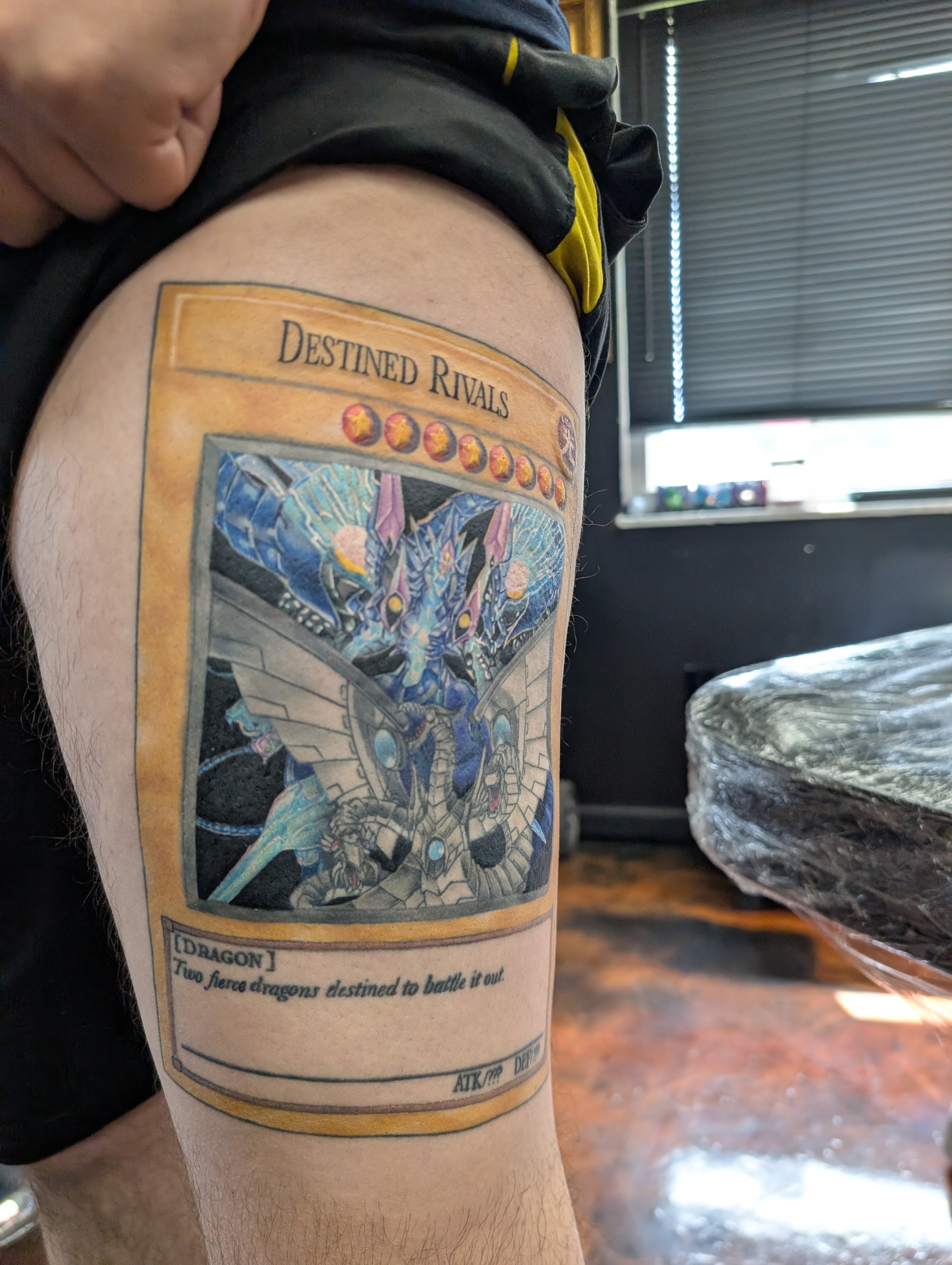 A tattoo on a person's upper arm featuring a dragon and a fantasy-style scene with colorful details, along with the text "Destined Rivals" and a quote about dragons fighting.