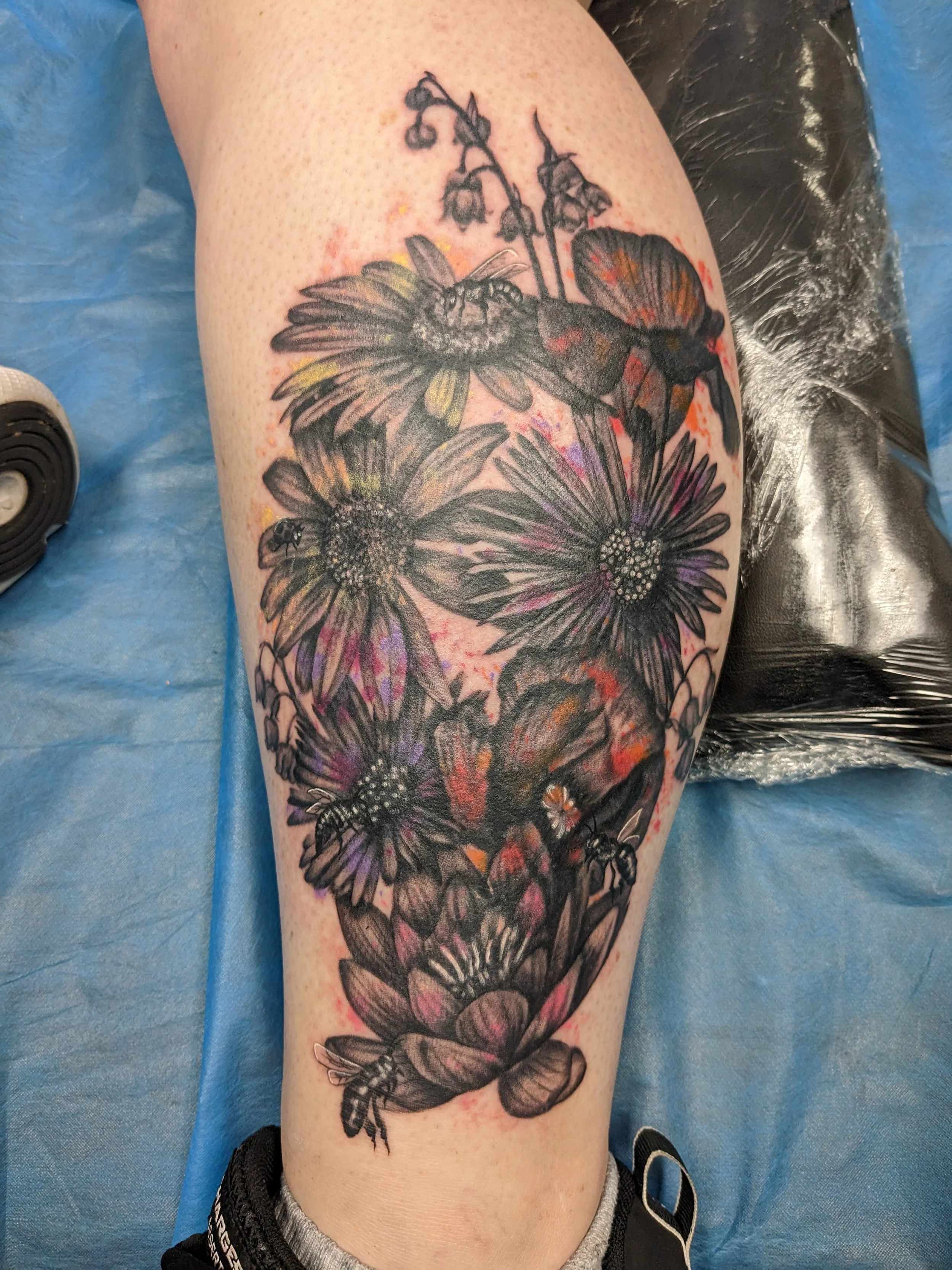 A tattoo of a bee, hummingbird, and flowers on a person's thigh.