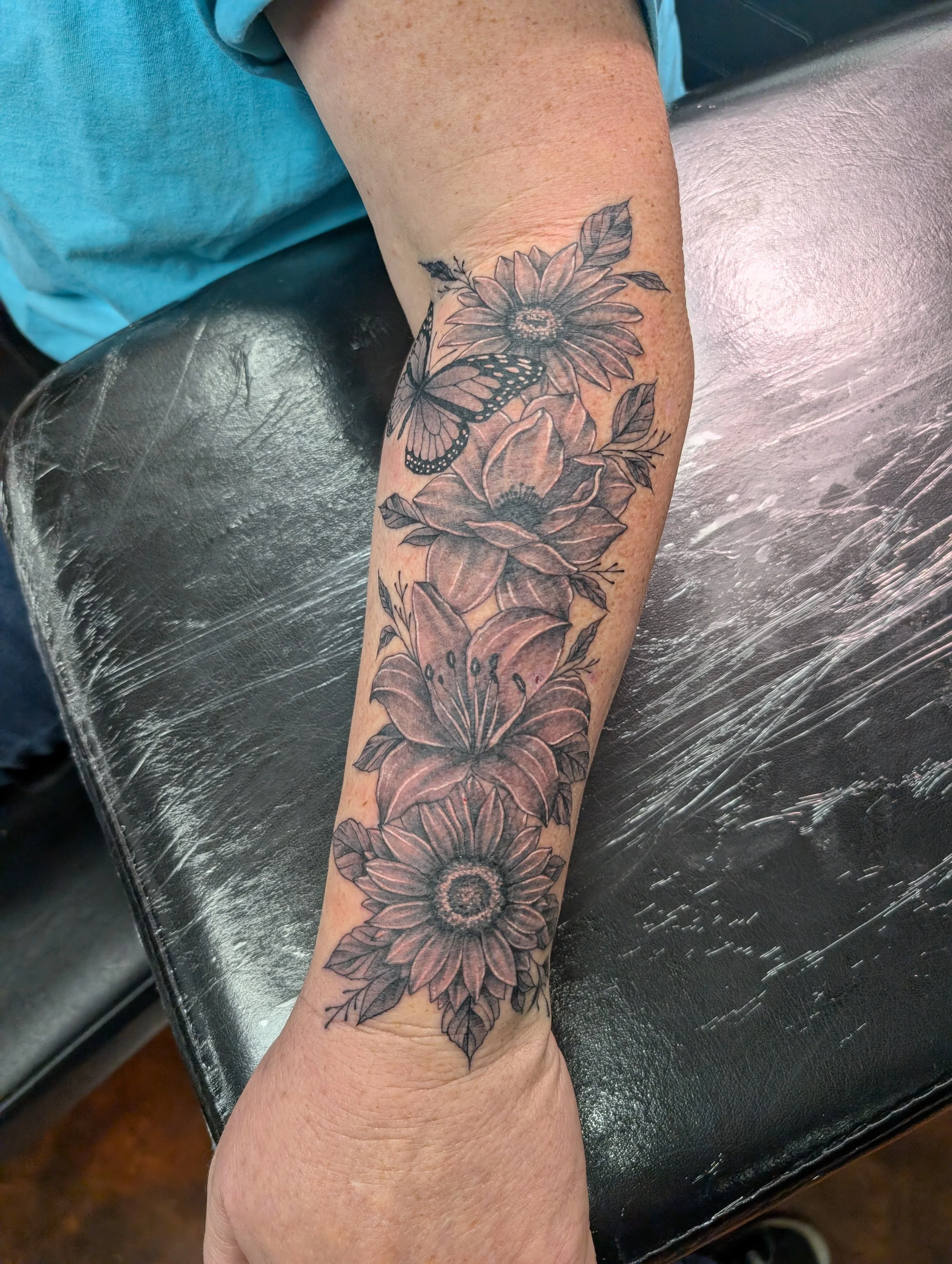 A person's forearm tattoo featuring large flowers and butterflies in black and gray ink.
