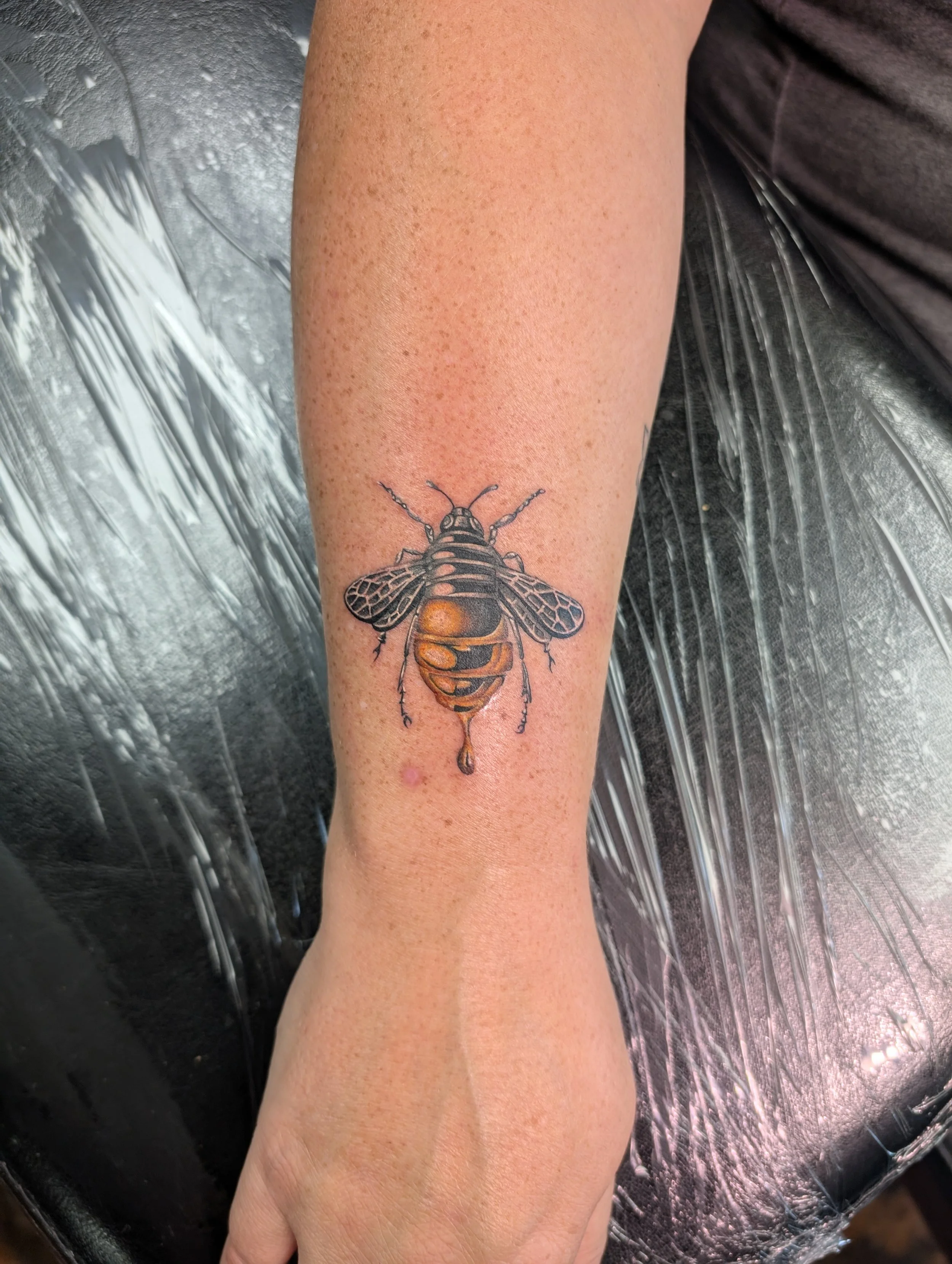 Close-up of a person's forearm with a detailed tattoo of a bee.