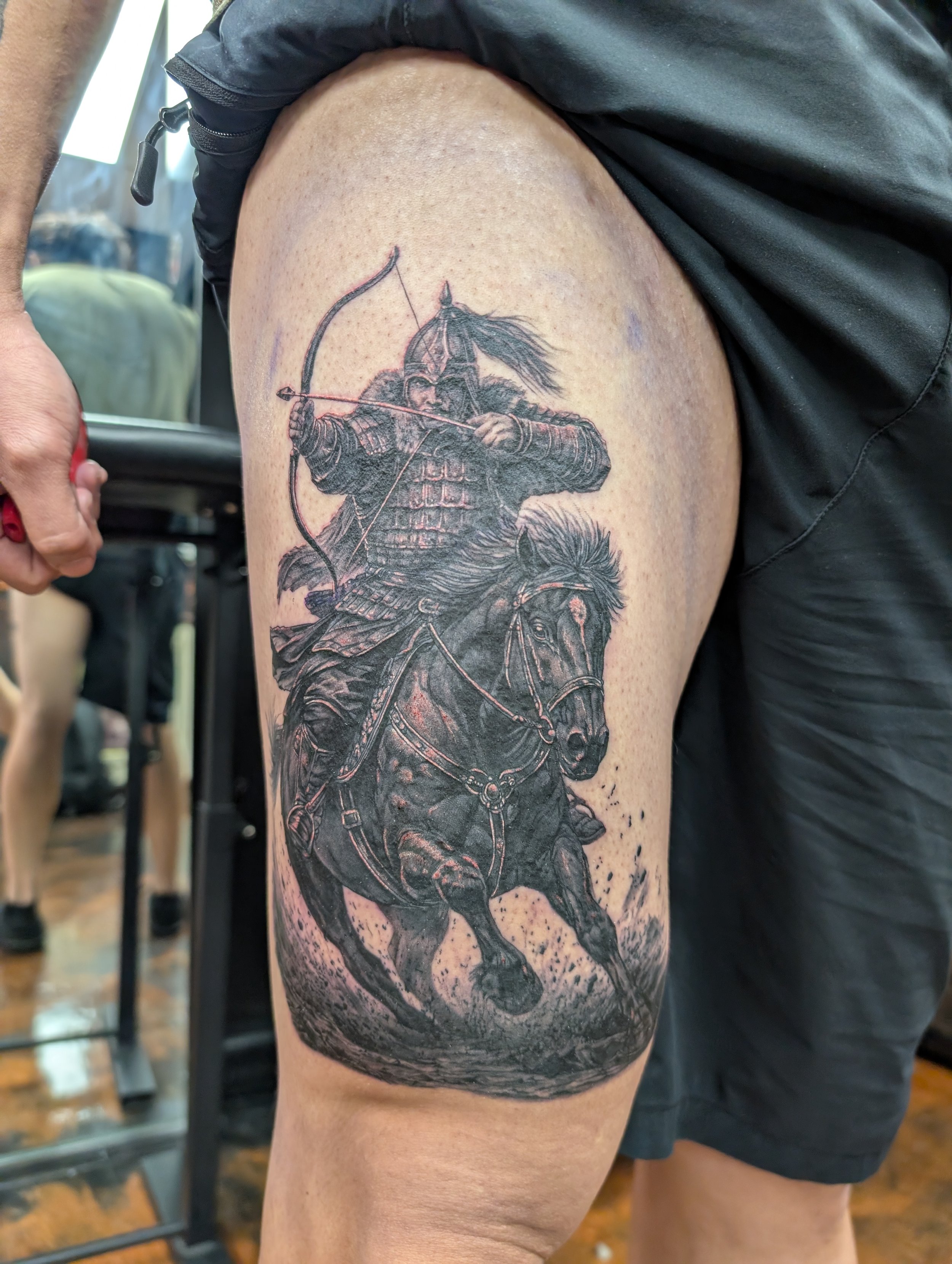 Tattoo of a medieval archer on a person's upper arm, depicting a soldier in armor aiming a bow and arrow, with detailed shading and a dark background.