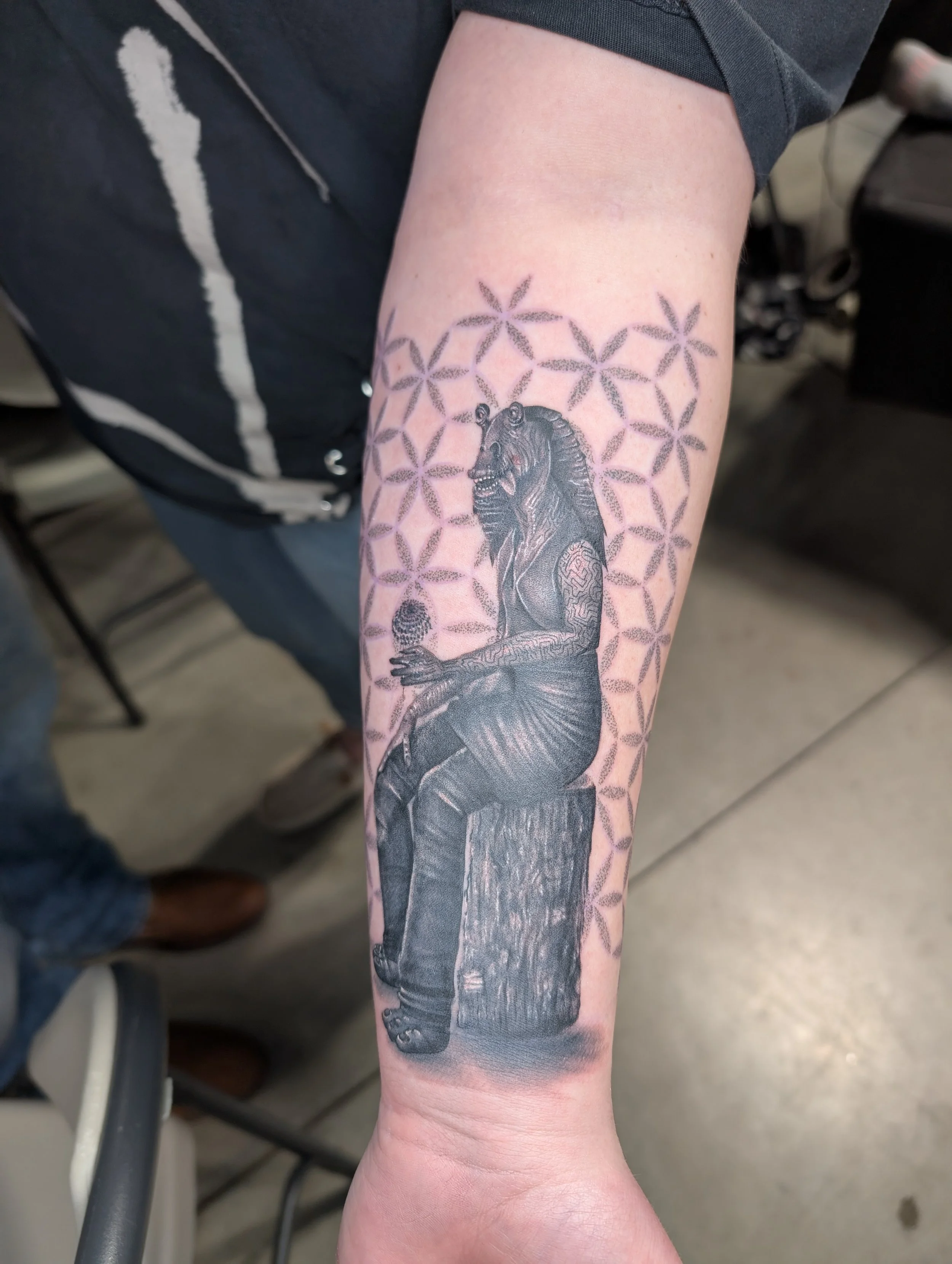 A tattoo of a Godzilla-like creature with detailed scales and a fierce expression, situated on a person's forearm.
