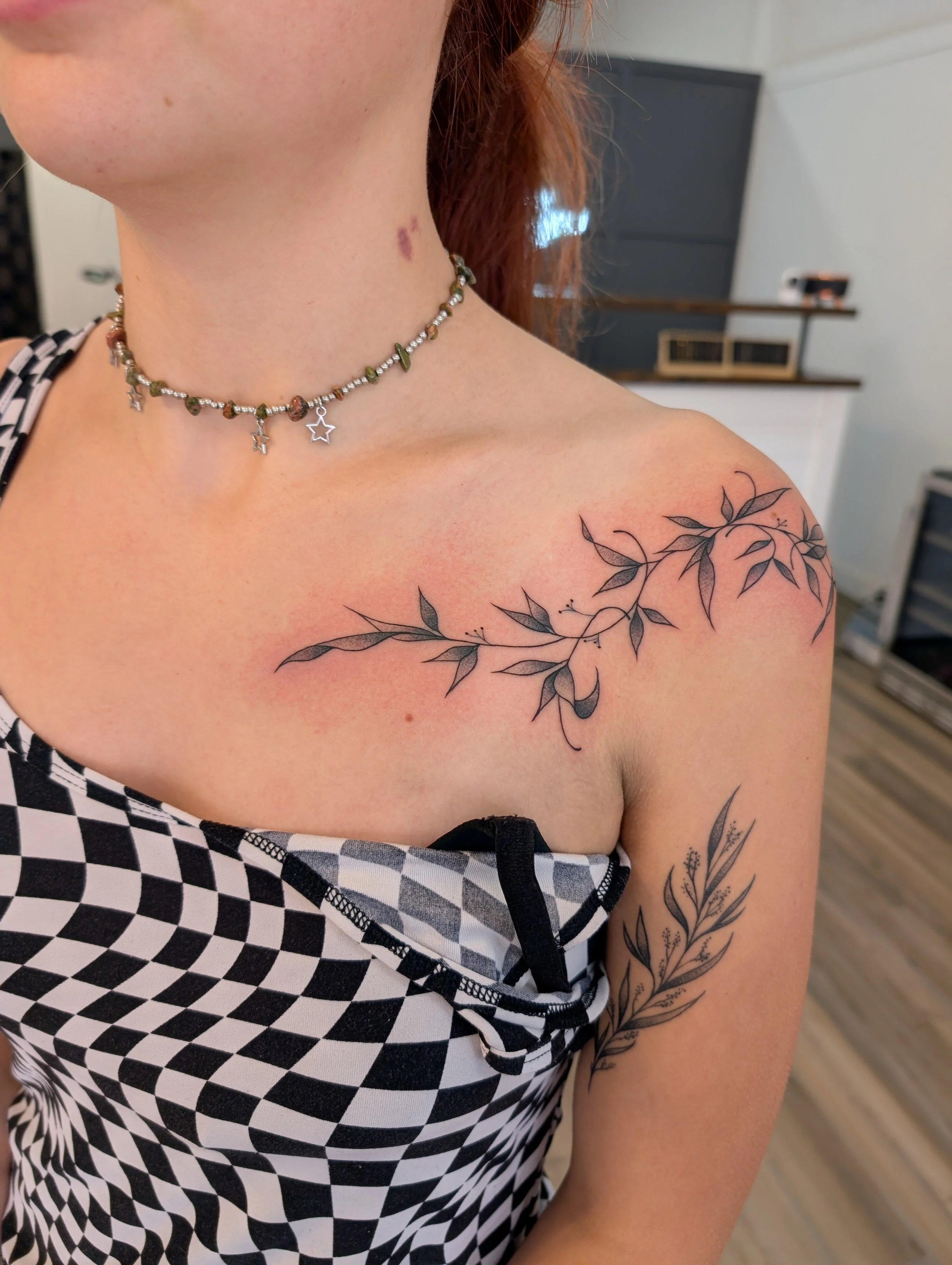 Close-up of a woman's shoulder, necklace, and arm tattoo with a black and white checkered top and background.