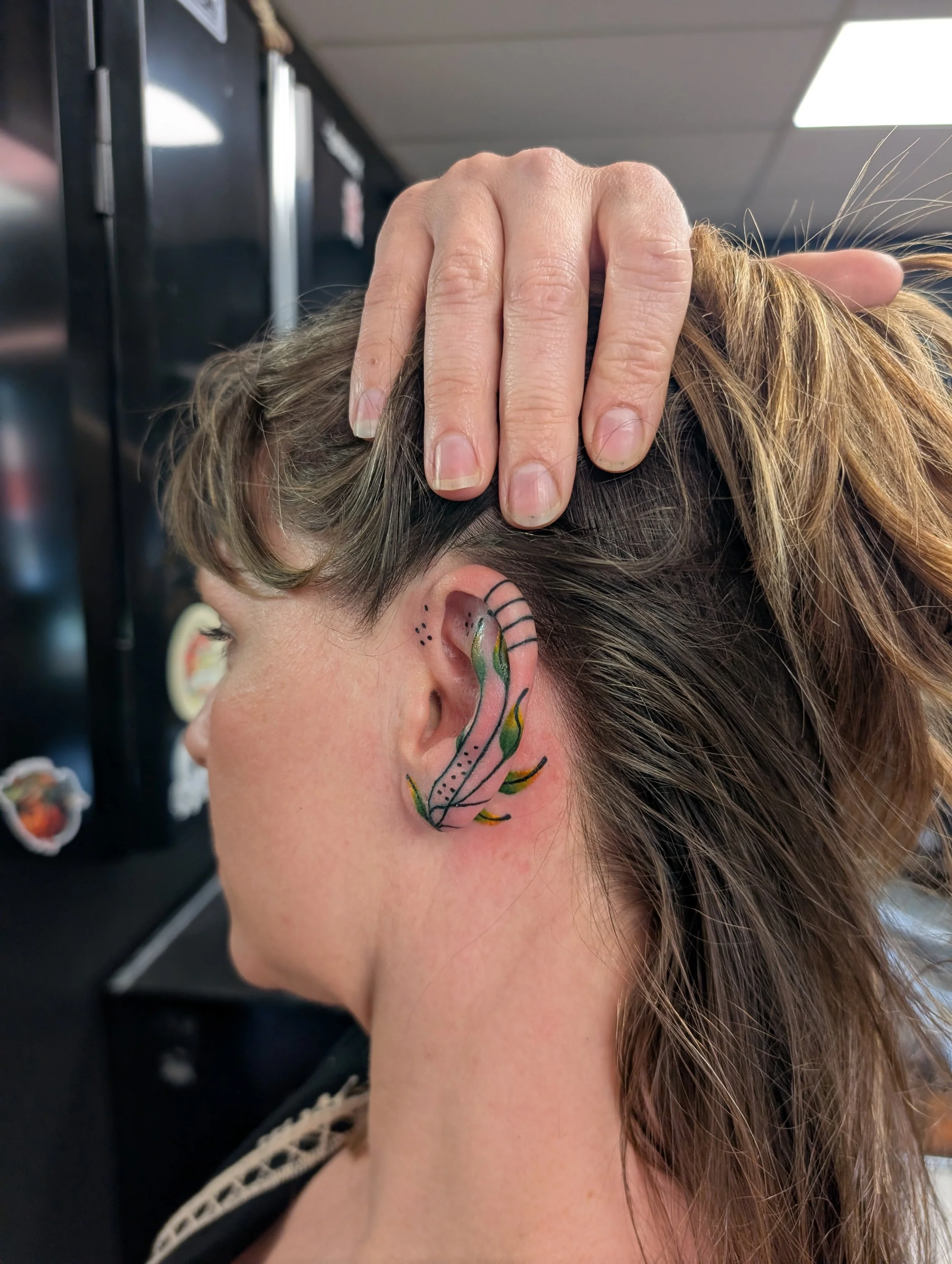 Close-up of a person with short, light brown hair and face painted with colorful botanical designs, gently holding their head with one hand.