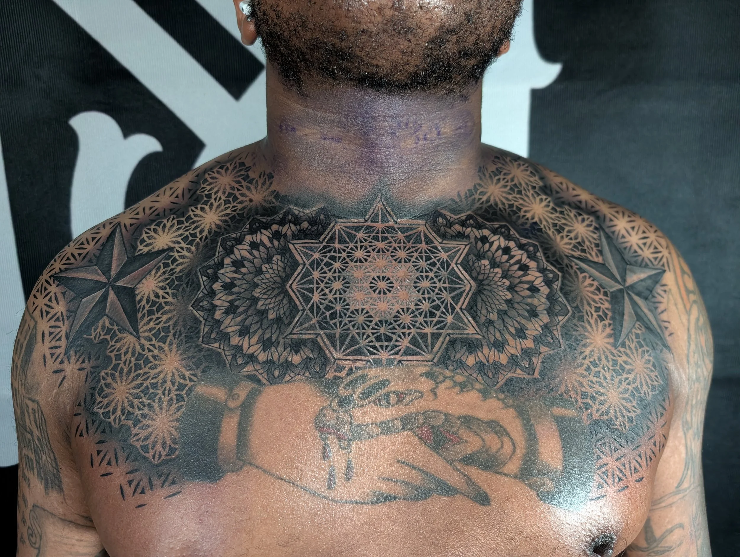 Close-up of a person's upper chest and neck, showcasing intricate geometric tattoo artwork and some scars or marks on the neck