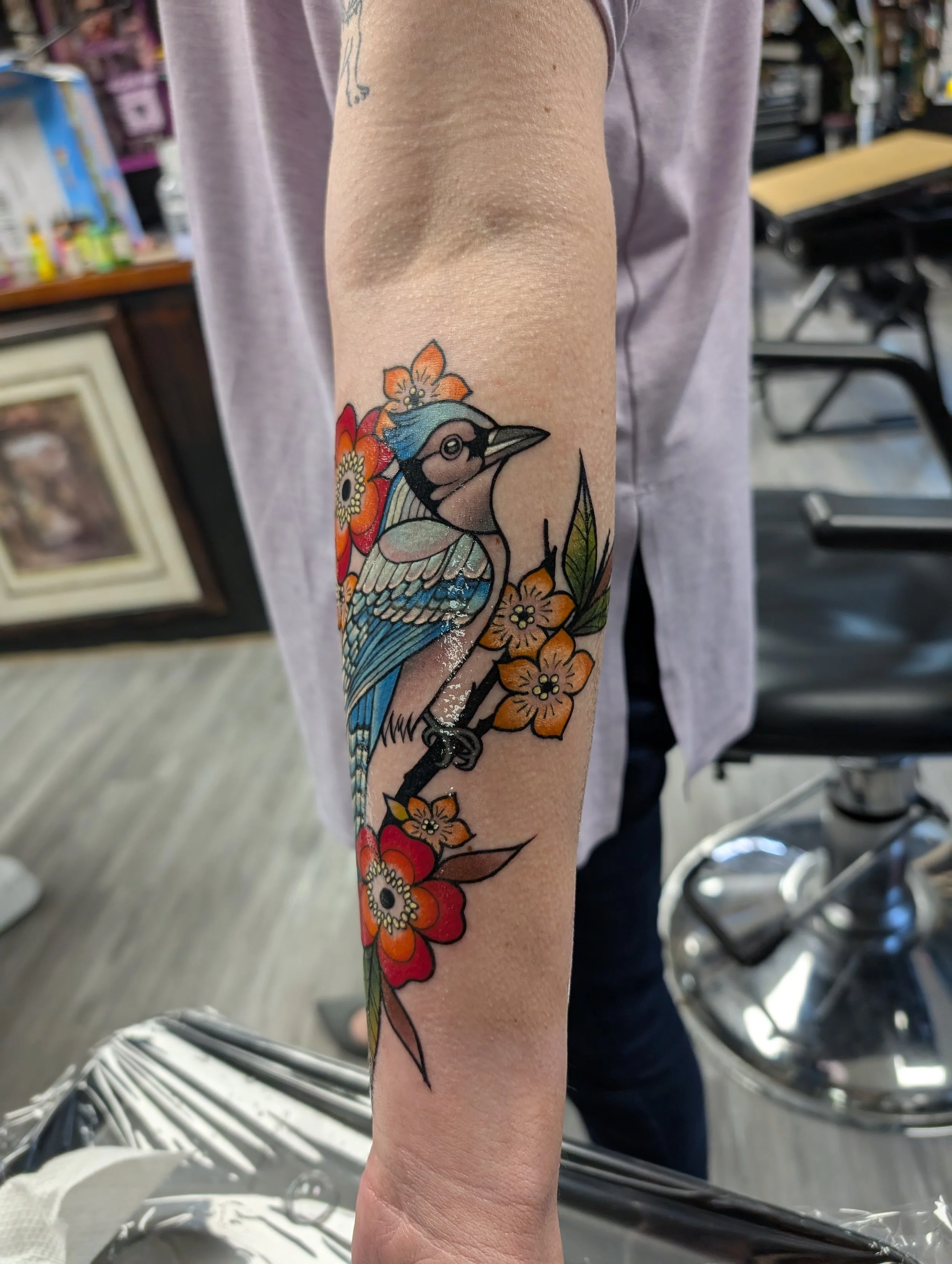 Colorful tattoo of a bird with flowers on a person's forearm in a tattoo shop.