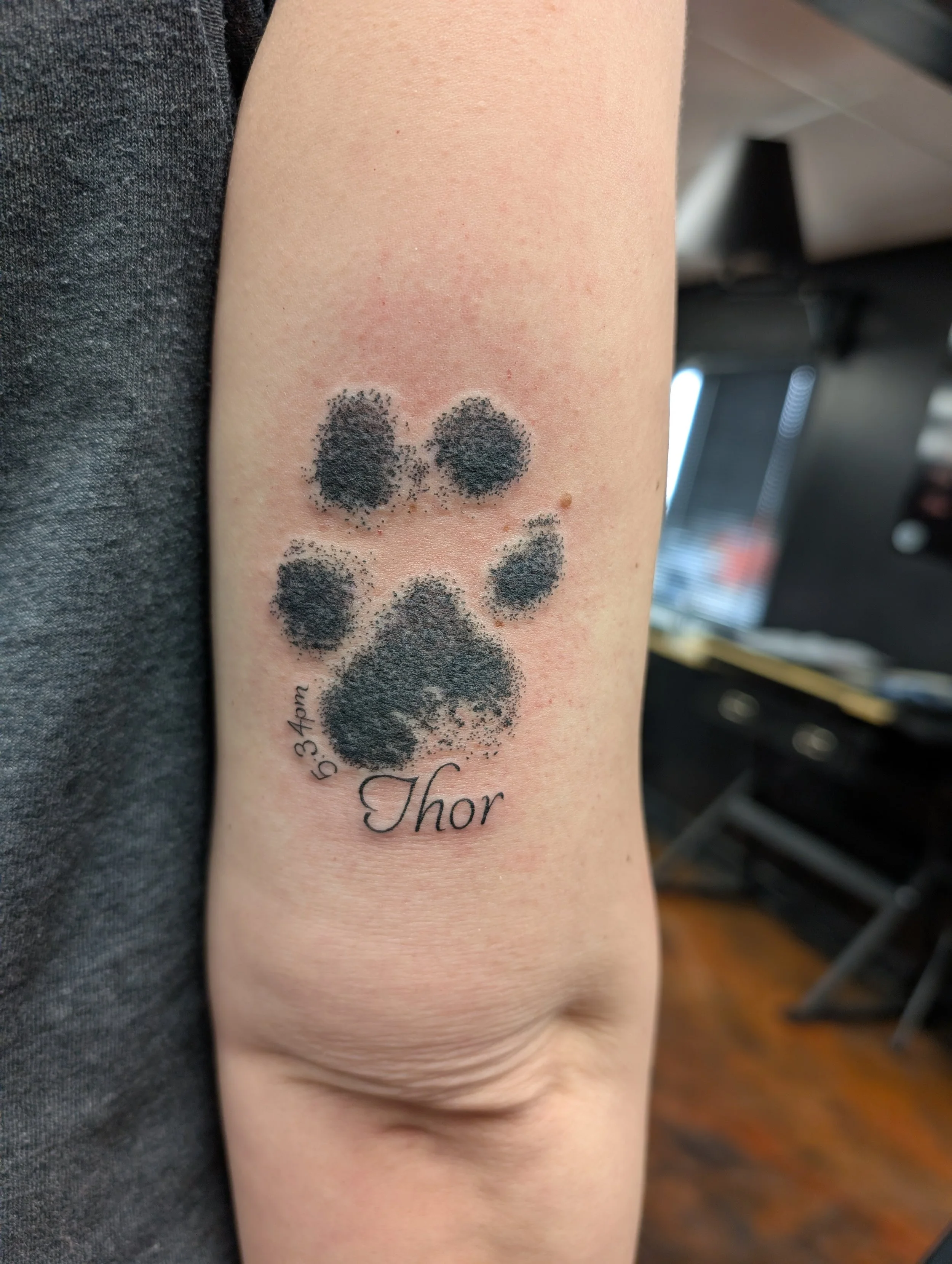 A tattoo on a person's arm depicting a smiling paw print with the name 'Thor' written below it.