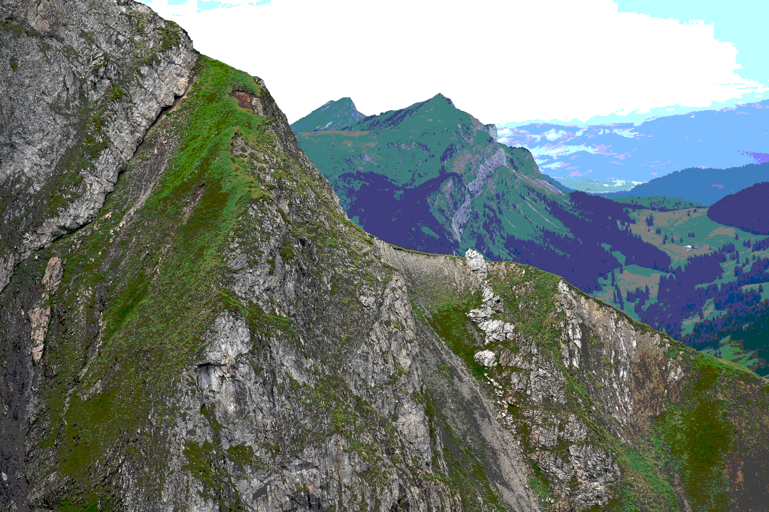 Auf einem felsigen Berg, mit grüner Vegetation, blickt man auf die umliegenden bergigen Landschaften mit grün bewachsenen Hängen und weiter entfernten Gipfeln unter einem am Himmel sichtbaren Himmel.