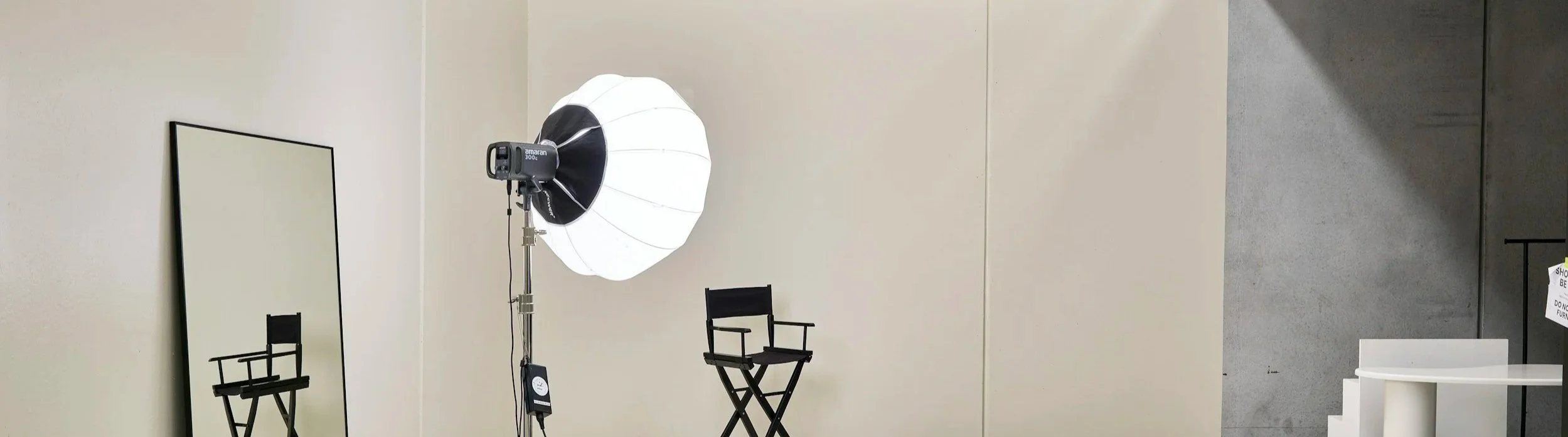 A photography studio setup with a large mirror, a director's chair, a softbox light, and some signage on a wall.