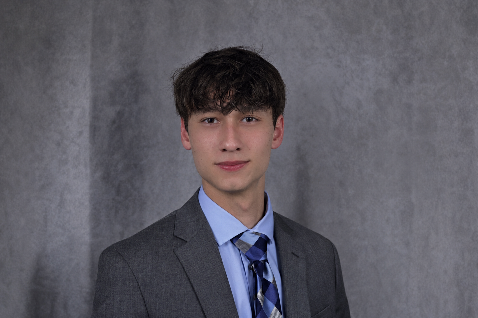 Young man in gray suit and blue tie against gray background