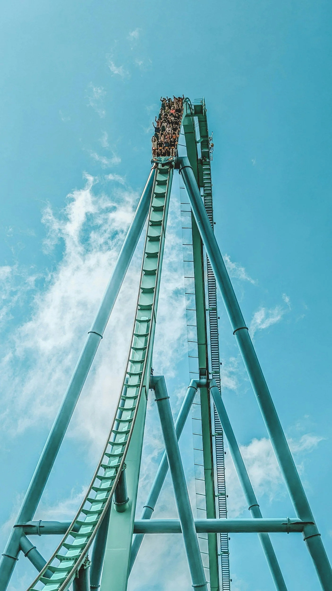 A tall blue roller coaster track against a partly cloudy sky with passengers at the top.