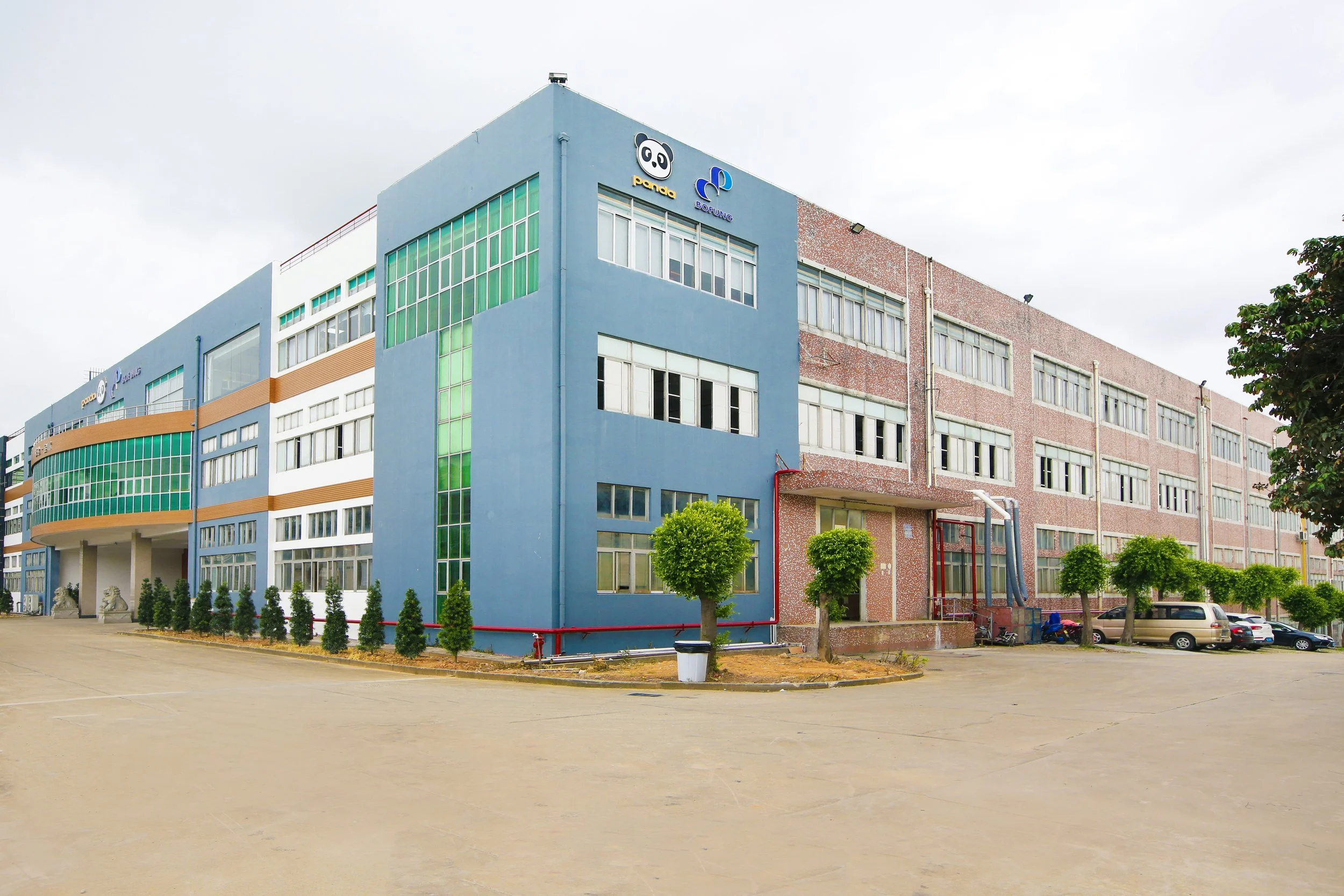 A large, colorful building with blue, pink, and white sections, decorated with panda and logo signs, surrounded by neatly trimmed green trees and parked cars, with an open paved area in the foreground.