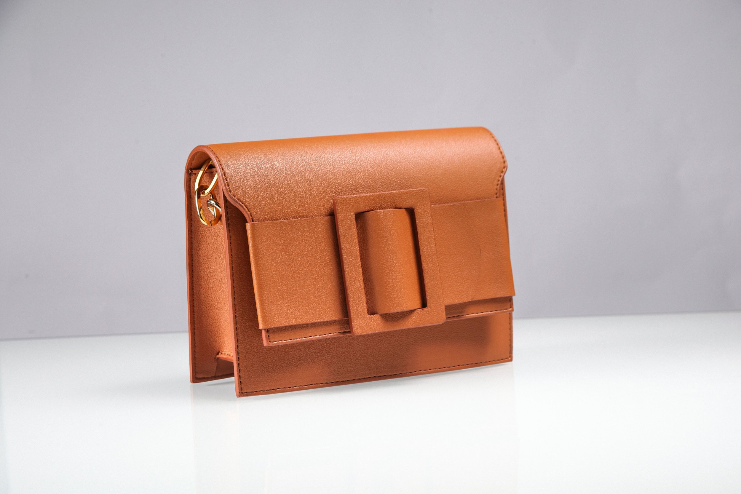 A brown leather handbag with a large buckle on the front, placed against a plain gray background.