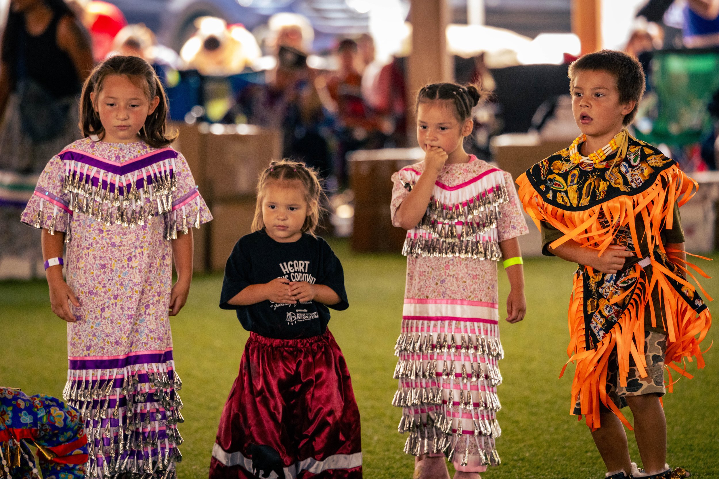 Children standing in line at a cultural festival, wearing traditional attire, with a festive background.