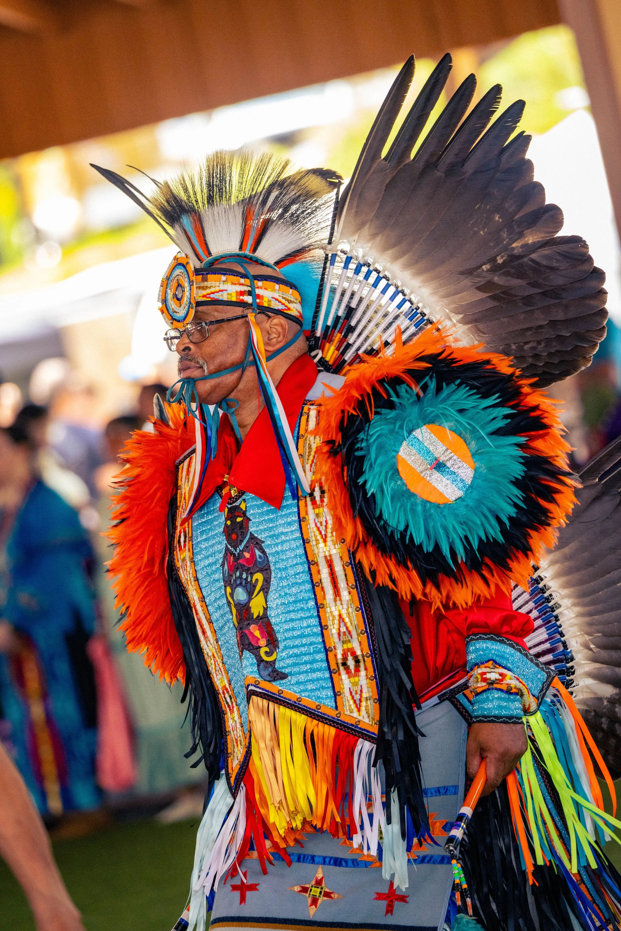A man wearing a colorful traditional Native American headdress and outfit, participating in a cultural event or ceremony.
