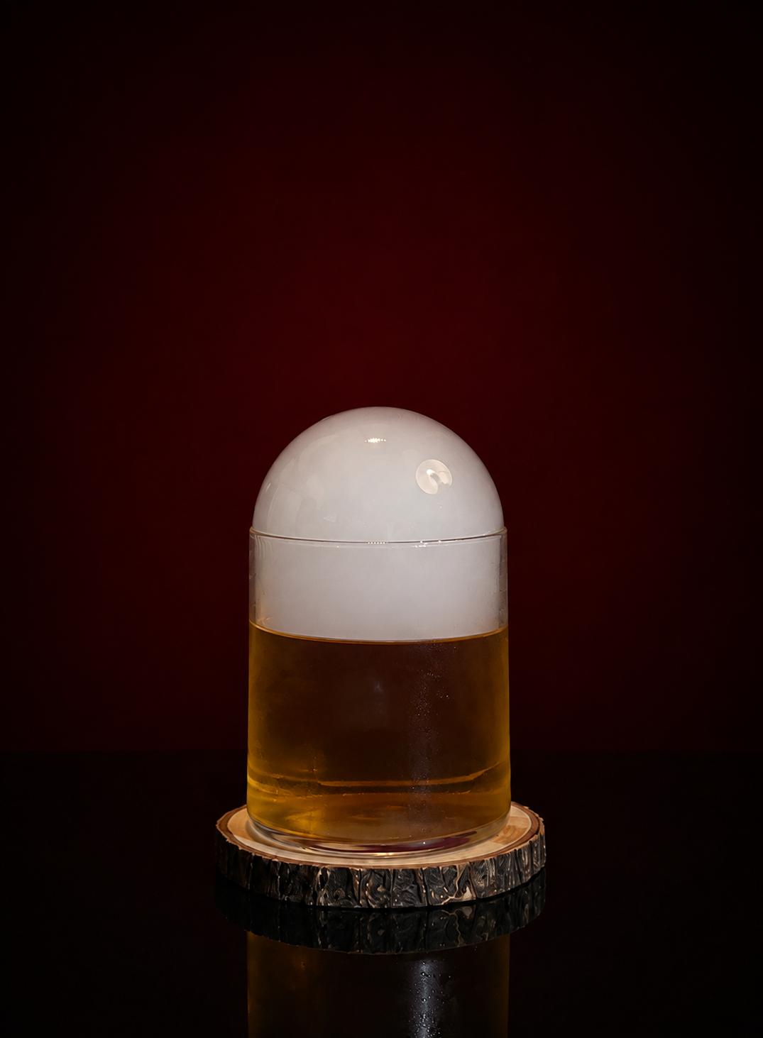 A cocktail with a white foam head, placed on a wooden coaster against a dark background.
