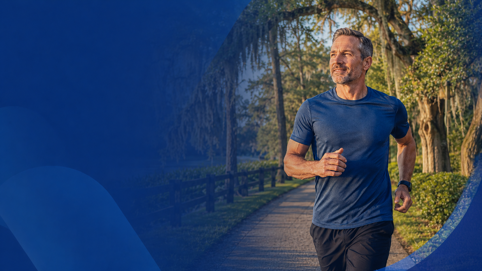 A middle-aged man jogging in a park during early morning, wearing a blue athletic shirt and black shorts, with trees and a pathway in the background.