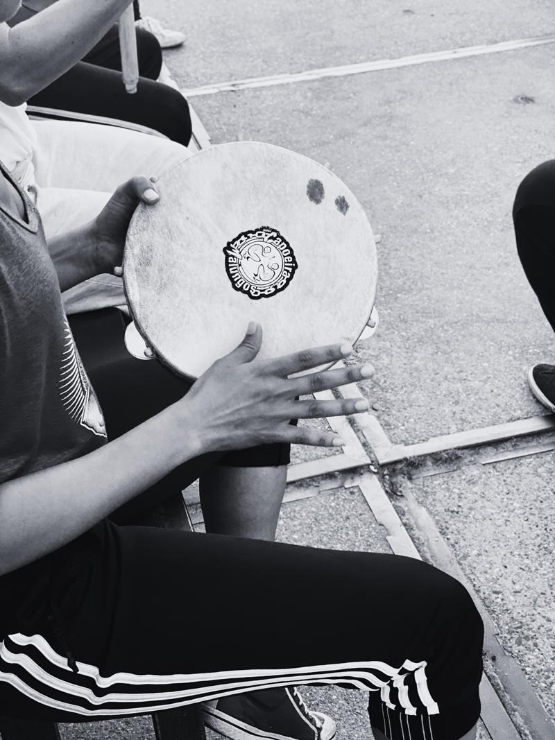 Person holding a small drum with a logo on it, seated outdoors on a bench.
