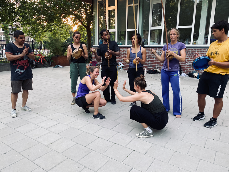 Group of people performing a traditional dance with percussion instruments outdoors.