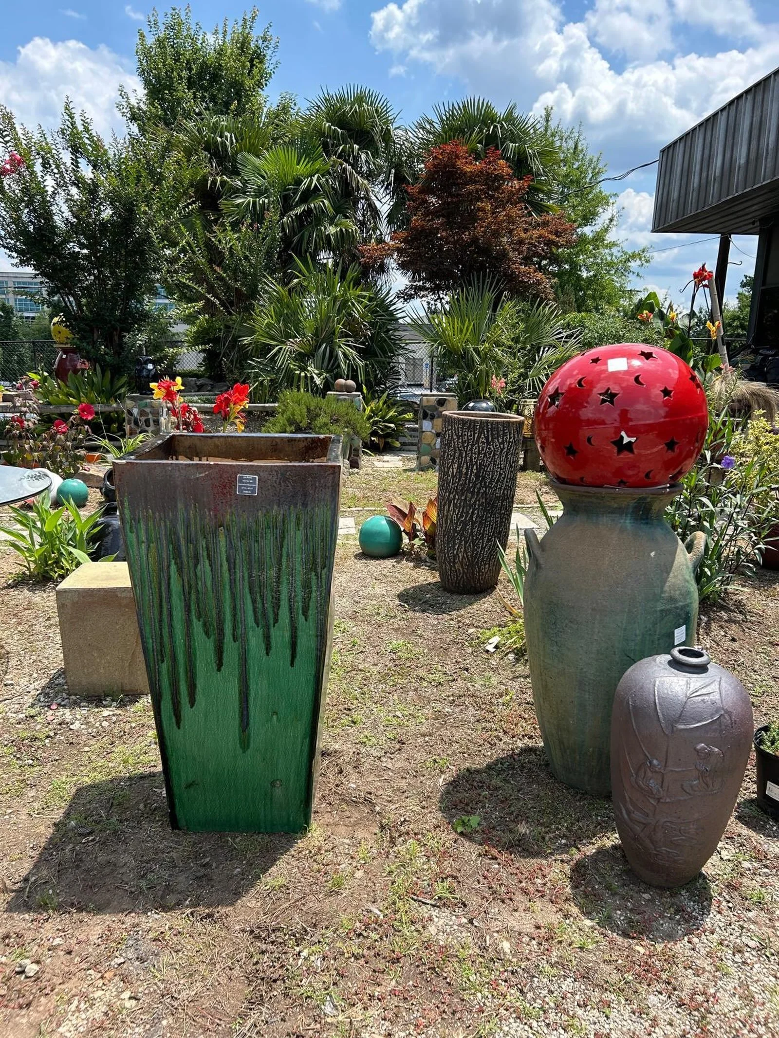 Under Carolina skies and palm shadows, the pottery tells its own story. Drip-glaze towers in deep green stand tall like forest guardians, while a fiery red gazing globe perched on an ancient urn catches the sun and waits to scatter stars across your 