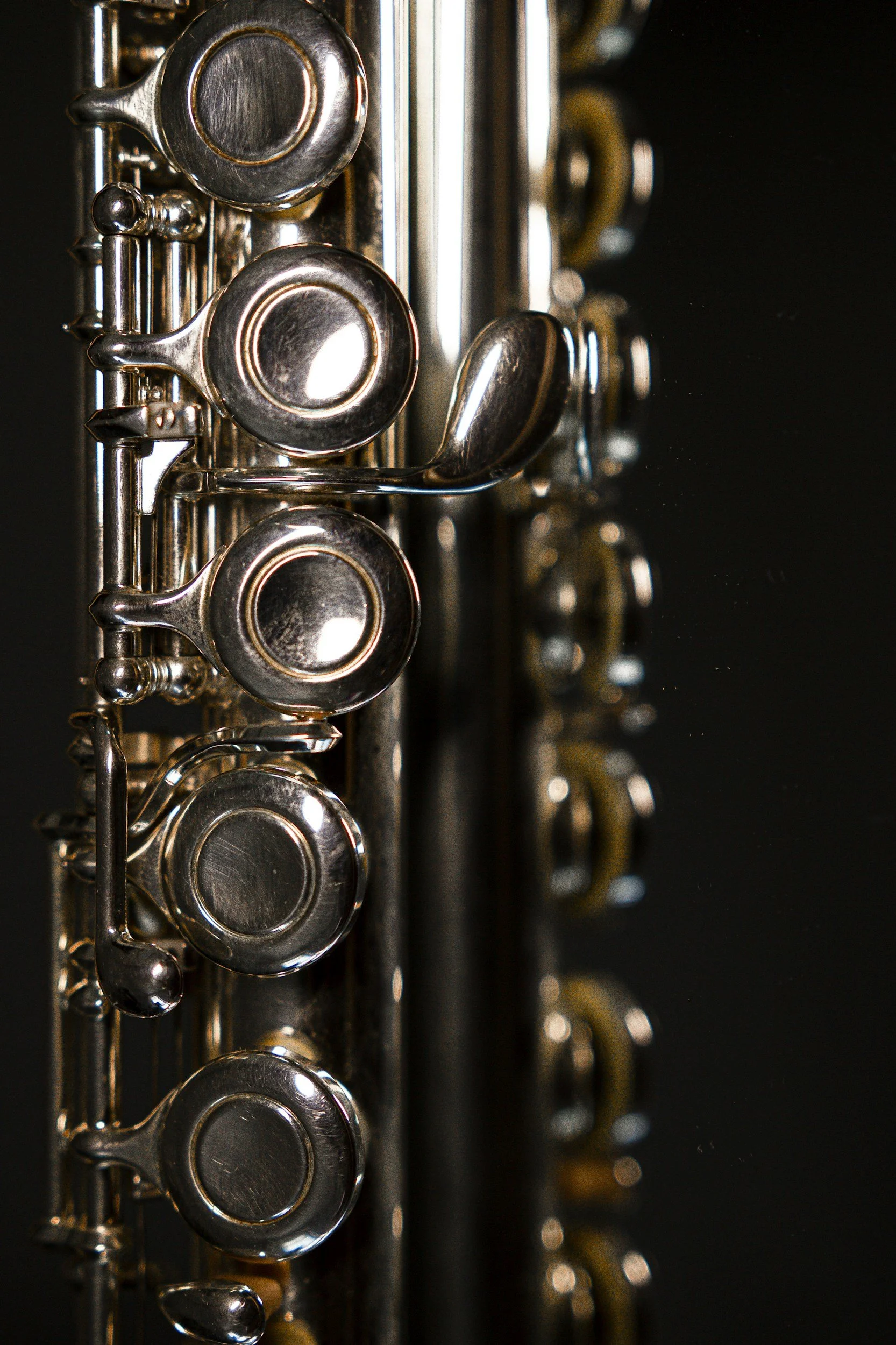 Close-up of a silver flute with the focus on the mouthpieces, reflecting light against a dark background.