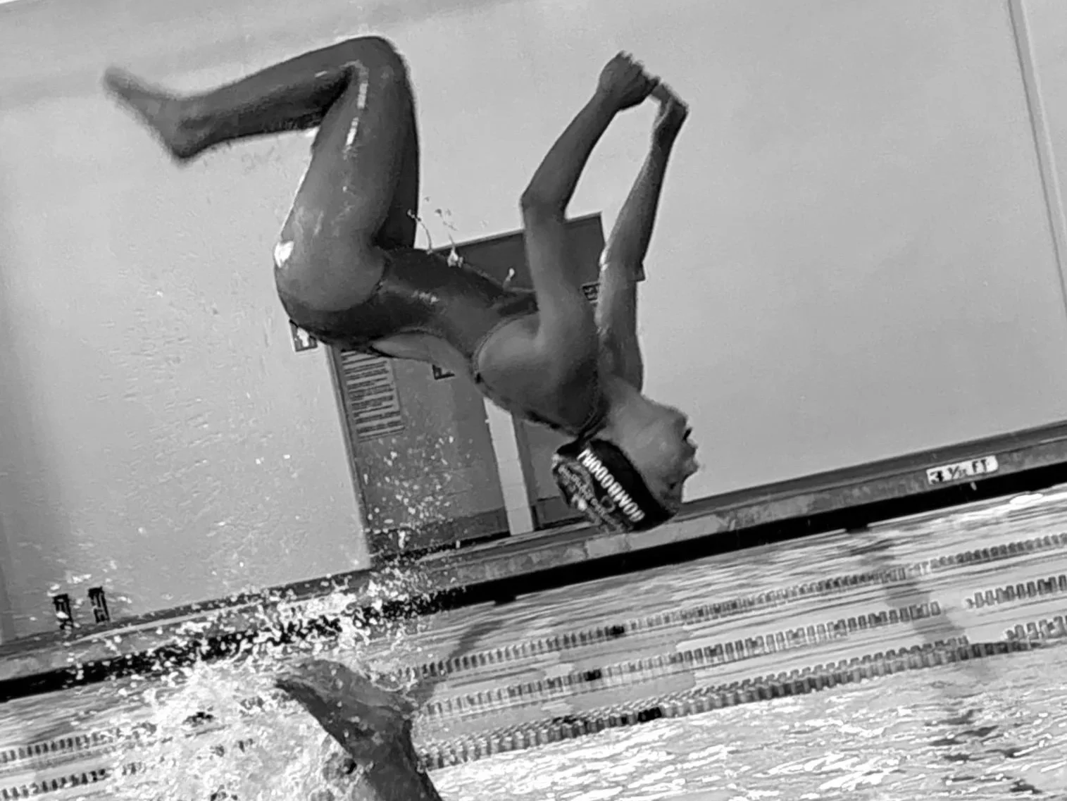 Female swimmer in a swimsuit and swim cap doing acrobatic artistic swimming in a pool