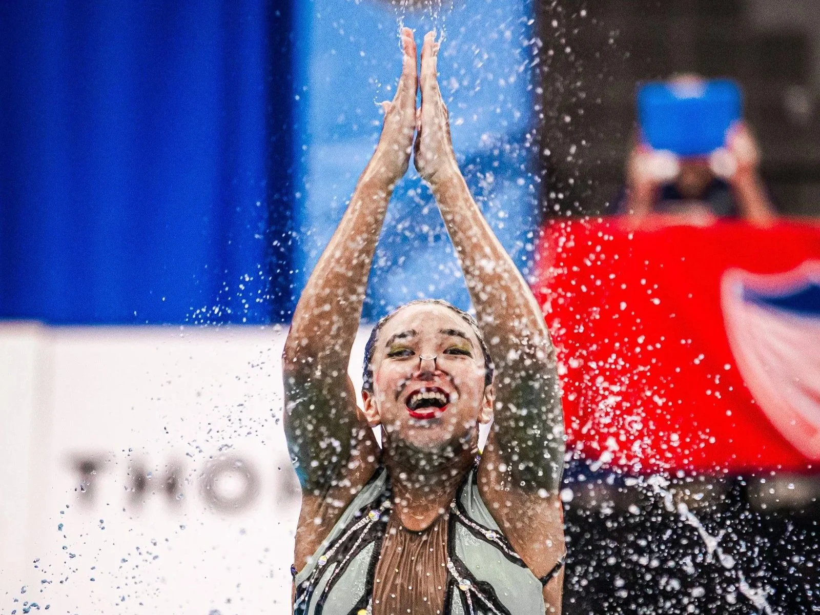 Swimmer smiling with hands in prayer position, water splashing around during an artistic swim competition in los angeles