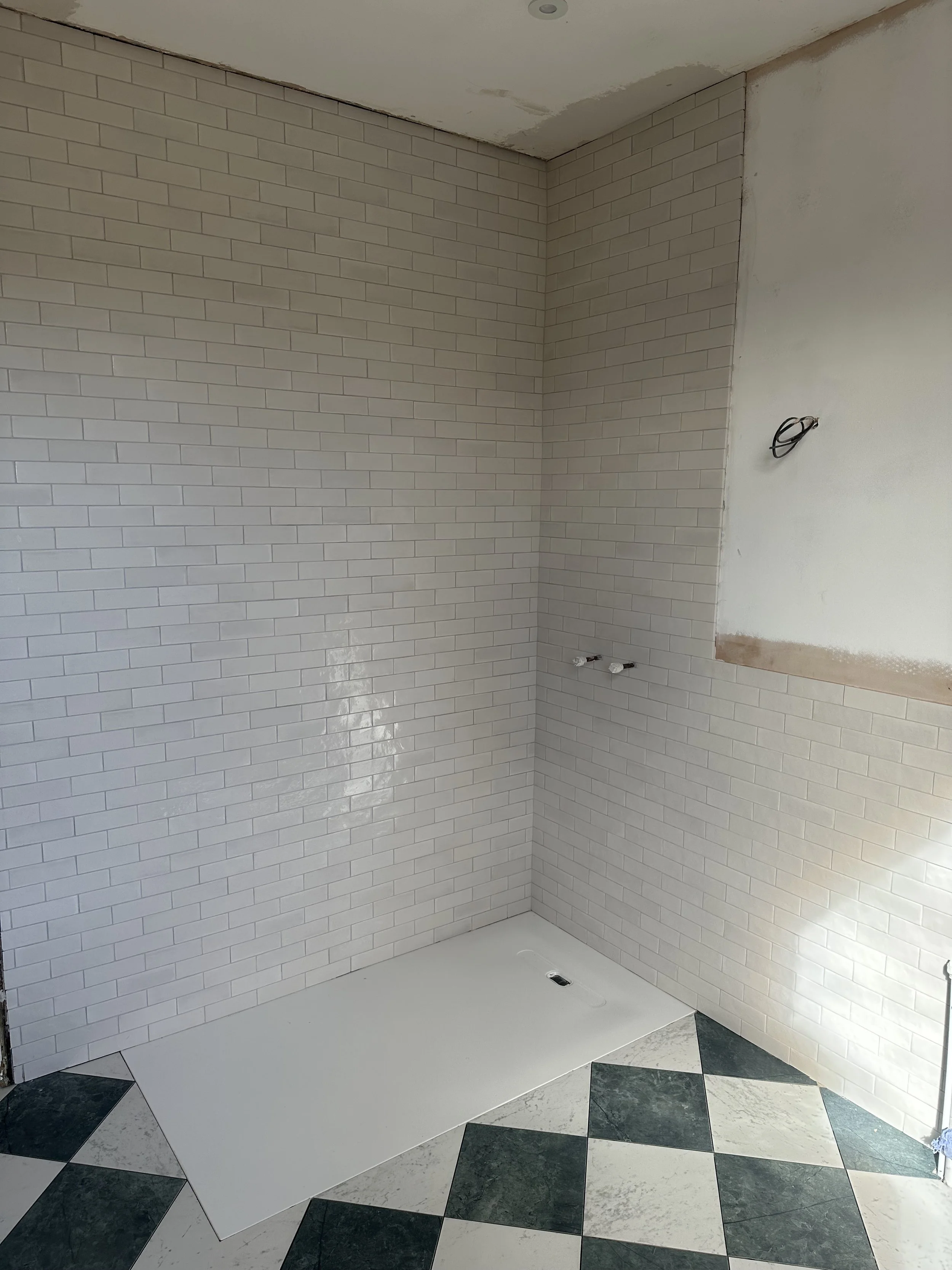 Interior of a bathroom under construction with tiled walls and checkered black and white floor tiles, electrical wiring visible on wall.