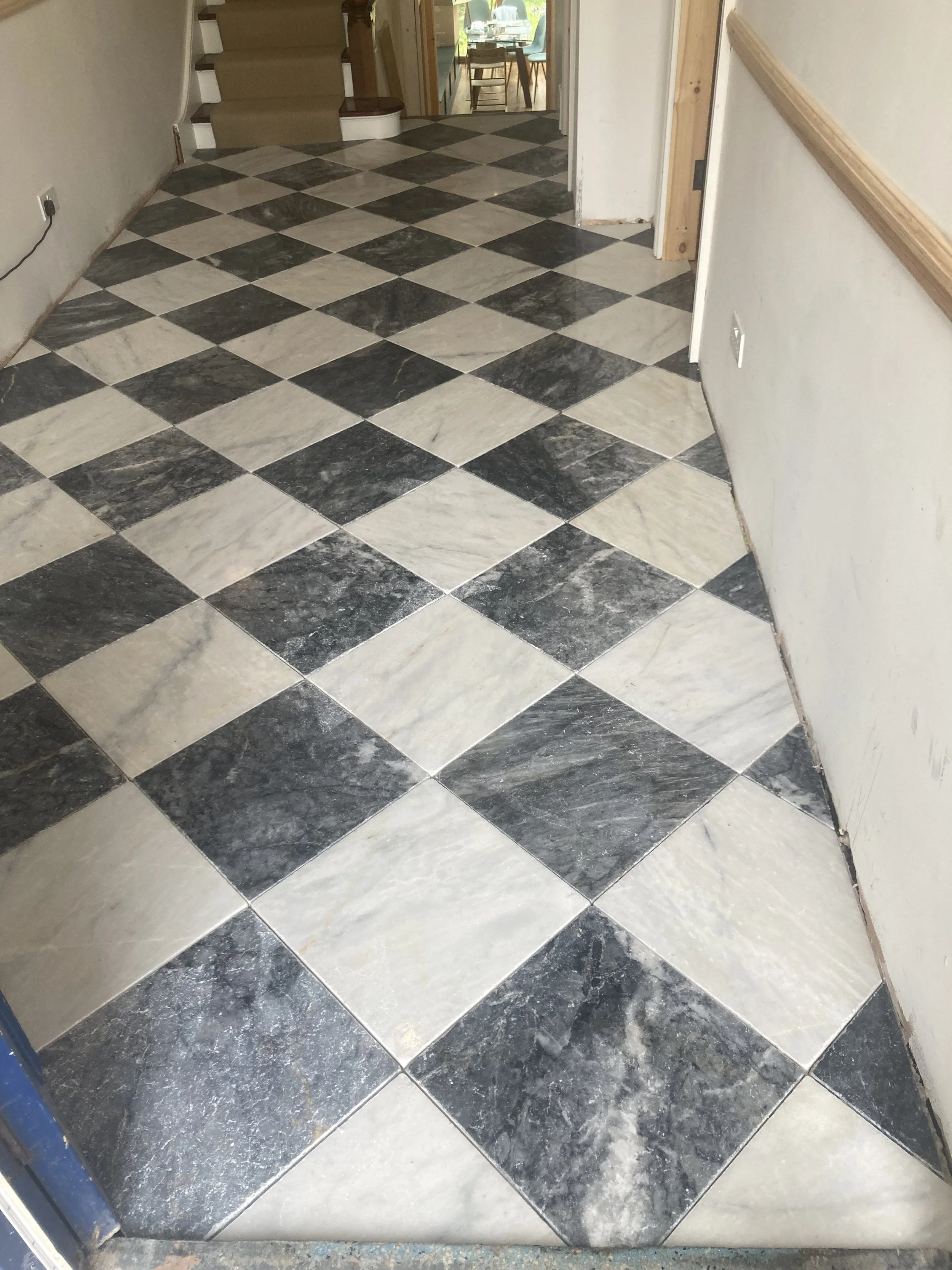Interior view of a tiled floor with black and white checkered pattern, adjacent to a wall and a staircase in the background.