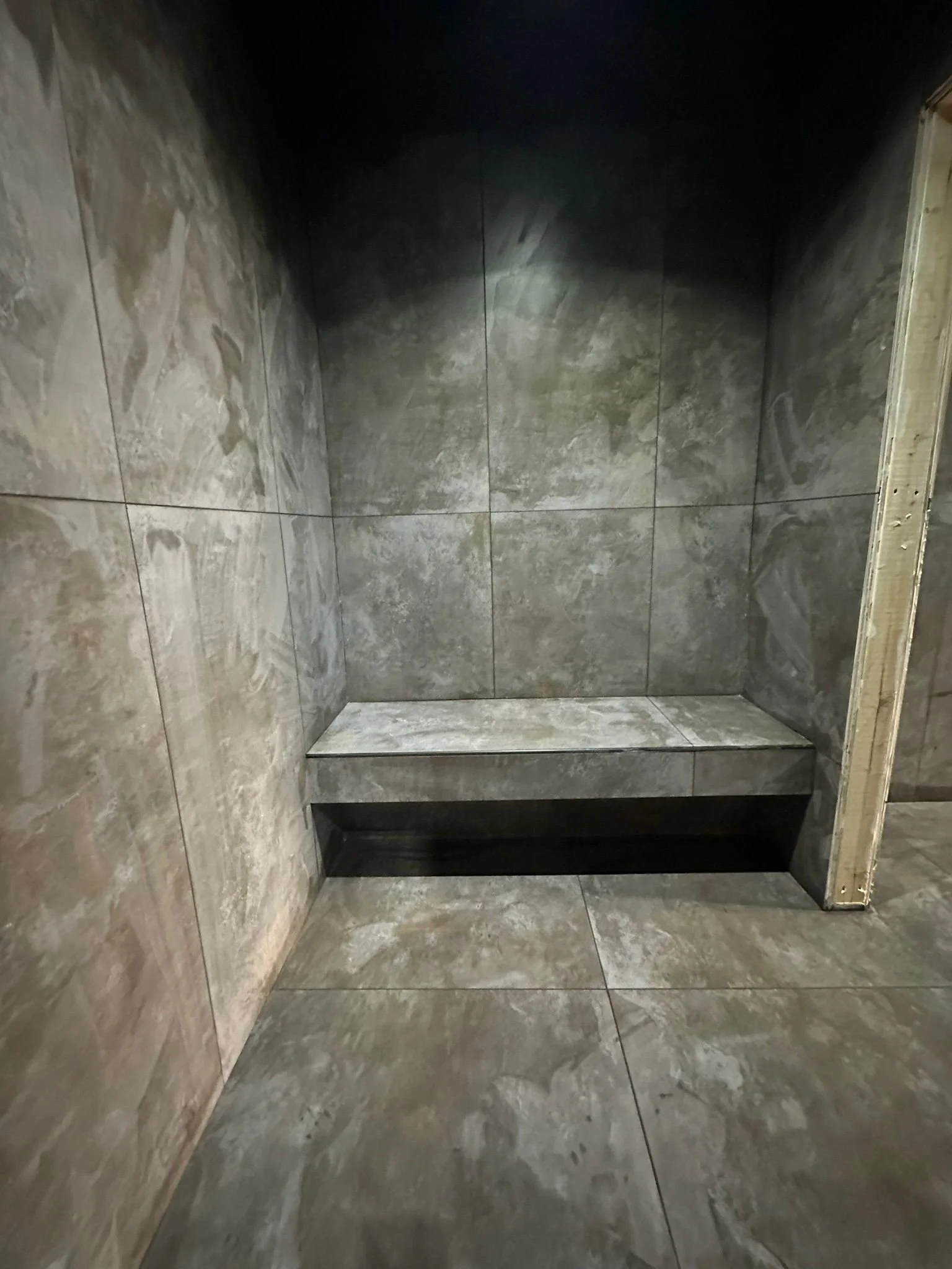 An empty shower area with gray marble tiles on the walls and floor, and a built-in bench on the left side.