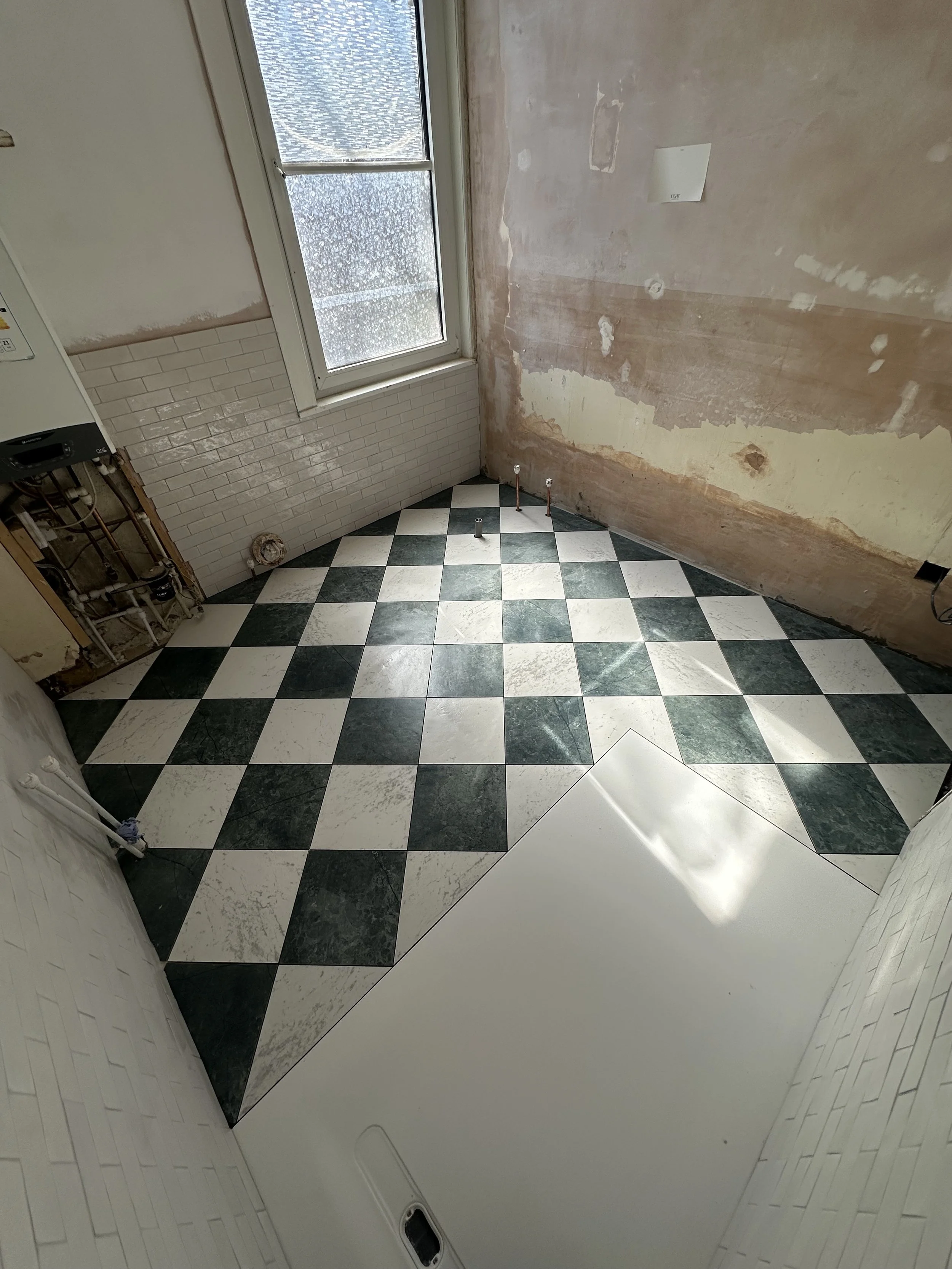 Room with black-and-white checkered floor tiles, partially removed wall covering, and exposed pipes and wall socket.