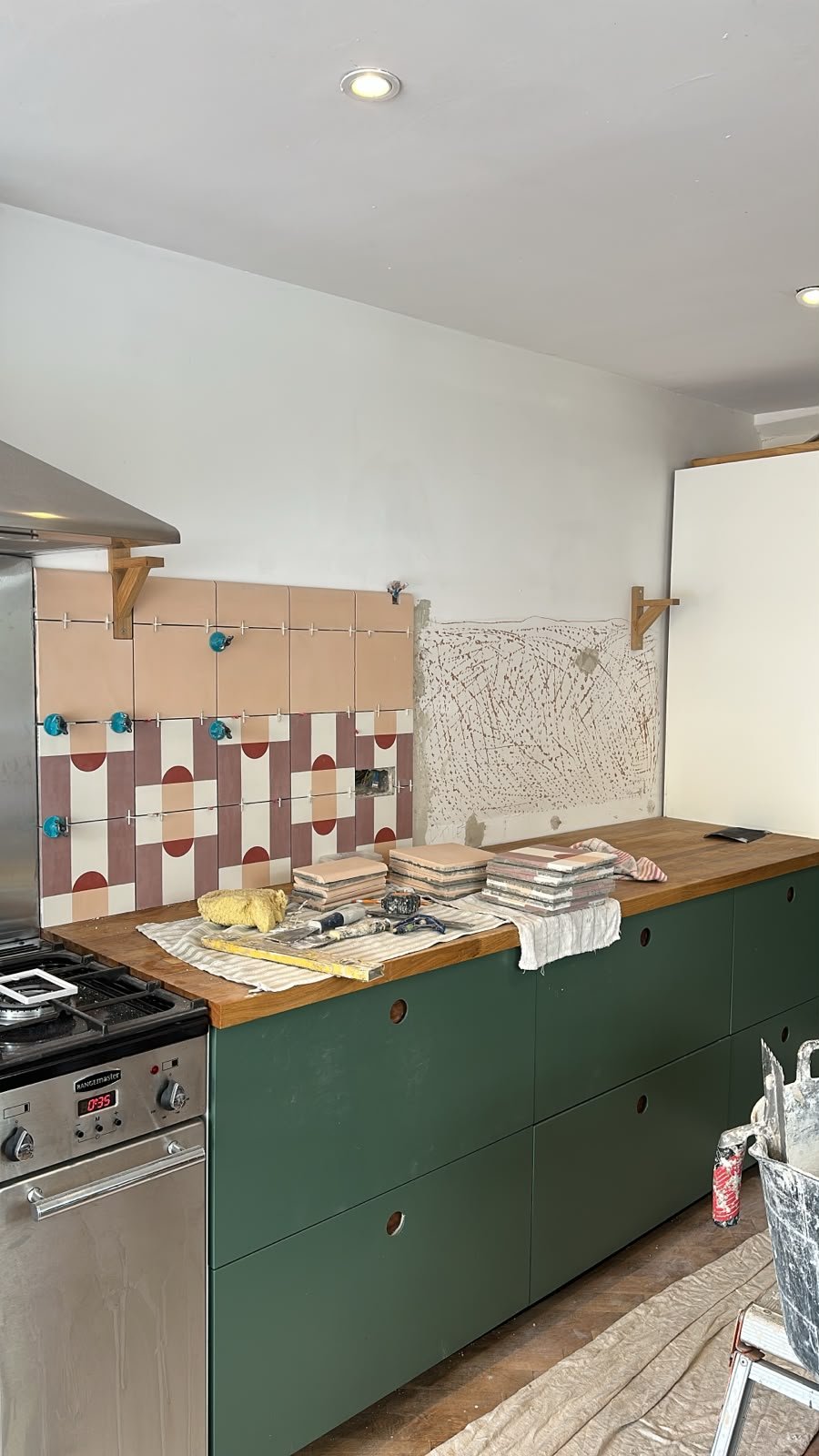 Partially renovated kitchen with green cabinetry, tiled backsplash, and construction materials on the countertop.