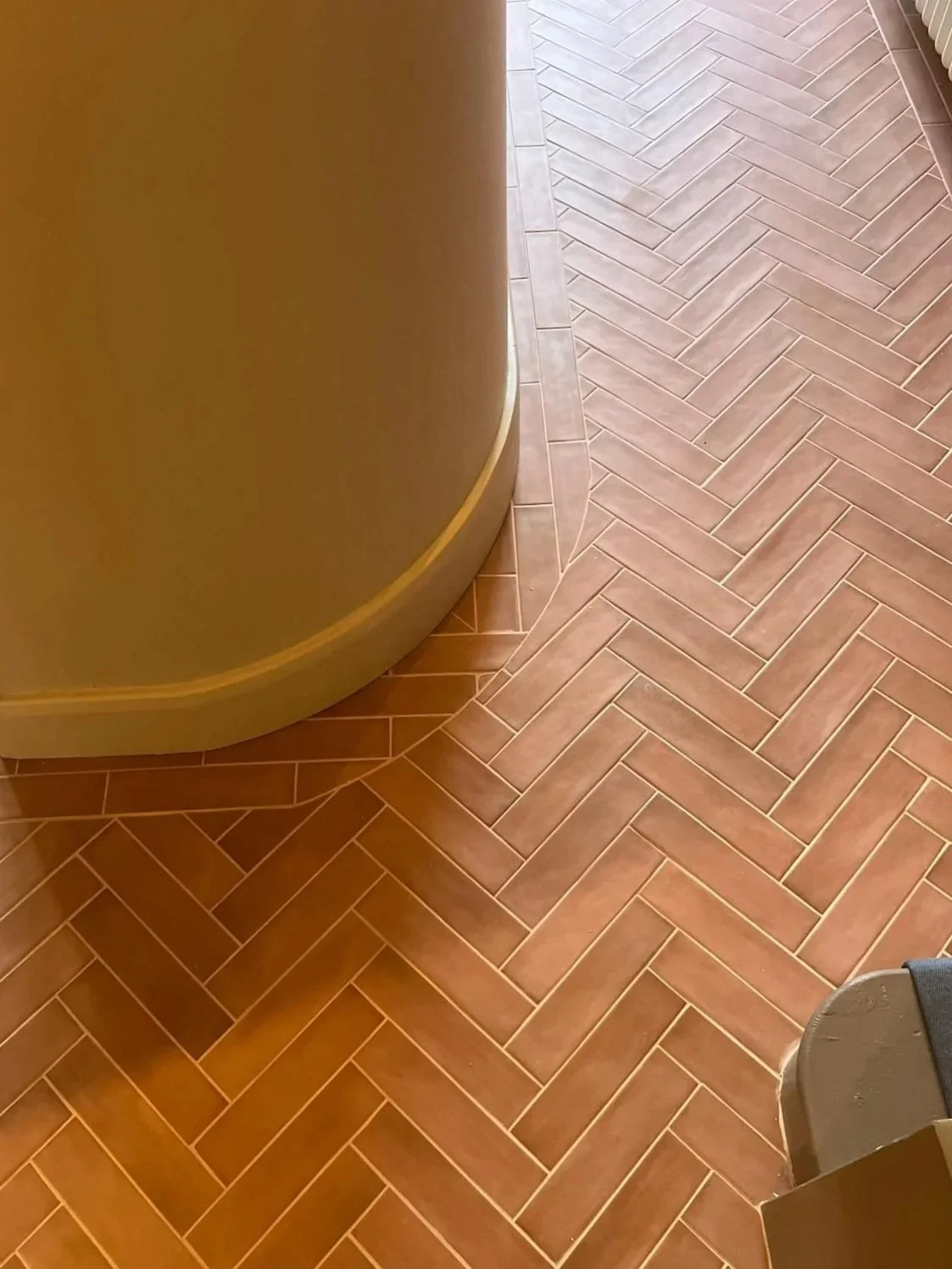Close-up of a corner with brown brick-patterned floor tiles and a beige curved wall.
