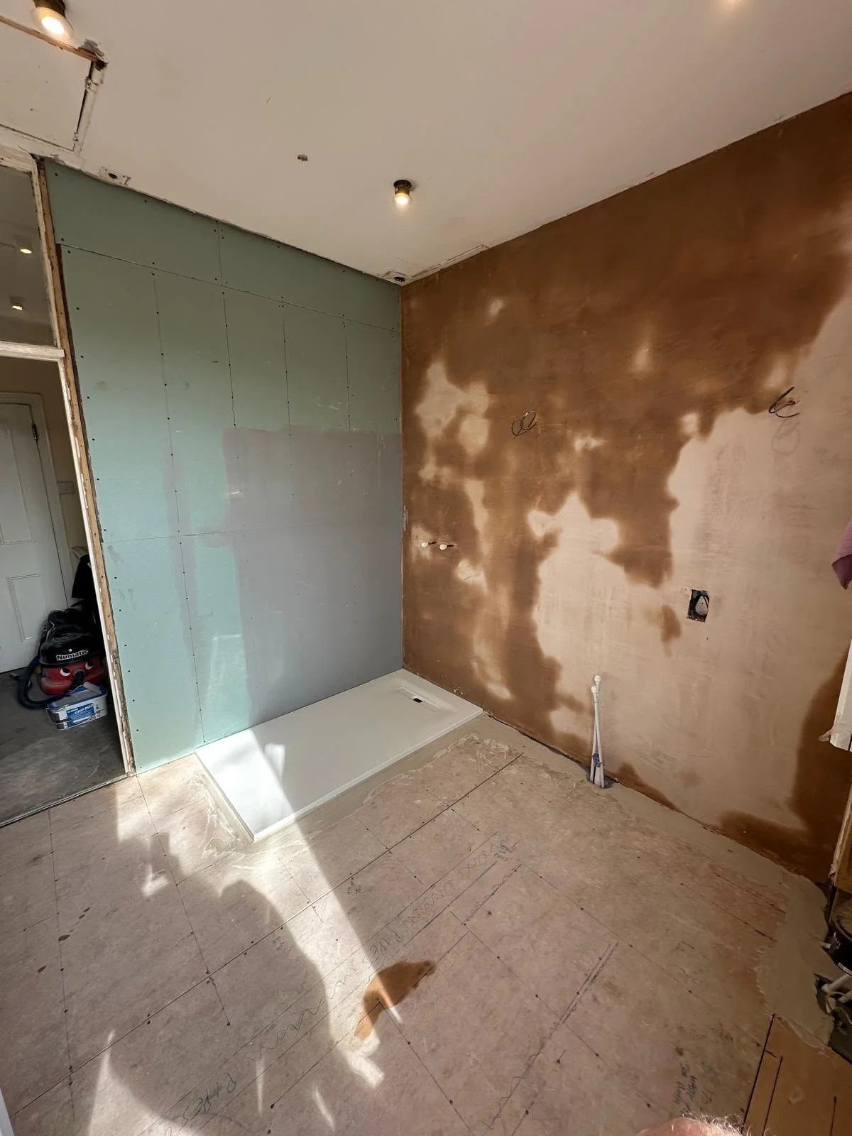 Room under construction with partially finished drywall, exposed wiring, and a new shower base installed on the floor.