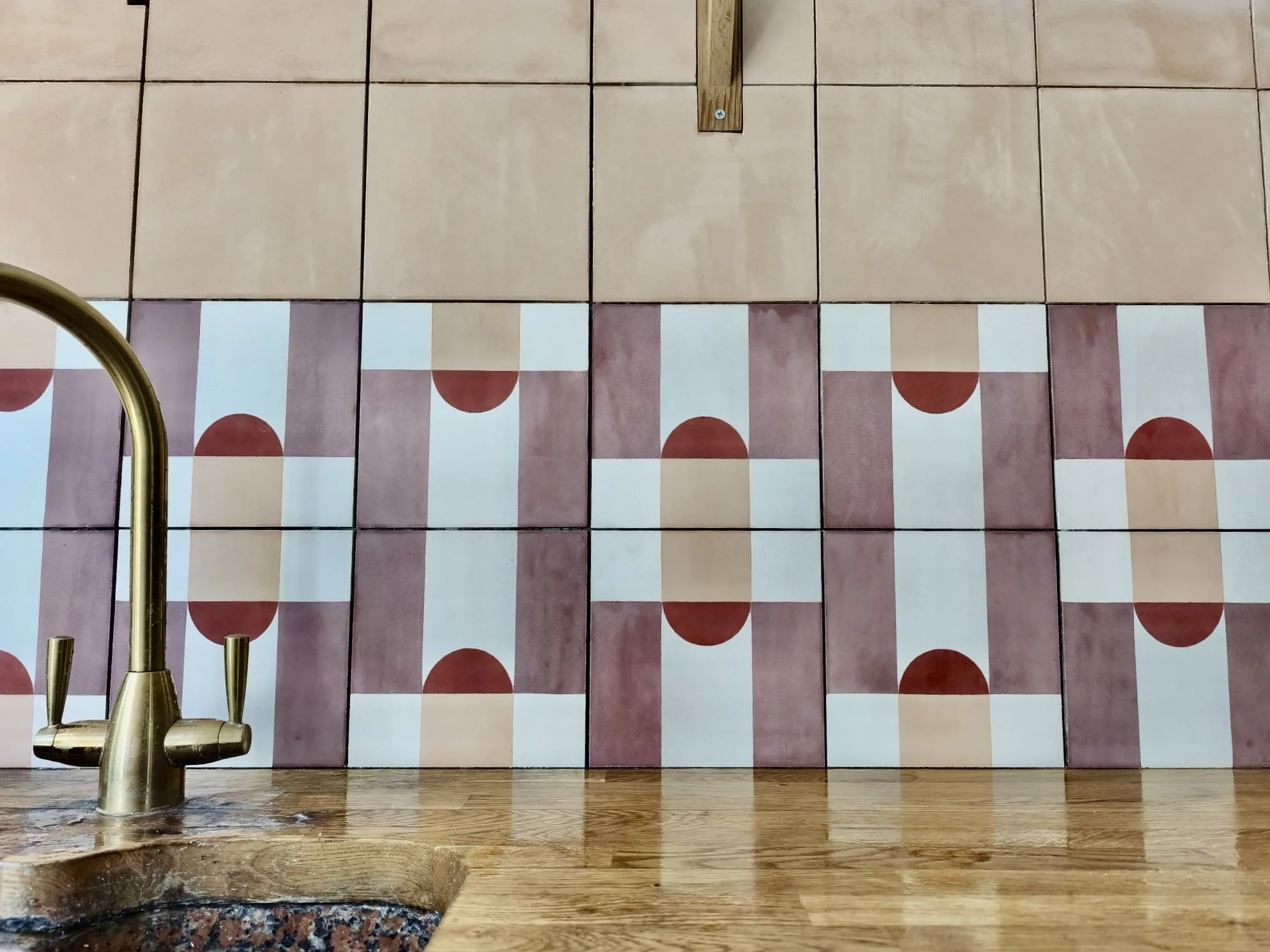 Close-up of a kitchen sink faucet with a tiled backsplash featuring alternating plain and patterned tiles in pink, white, and red colors.
