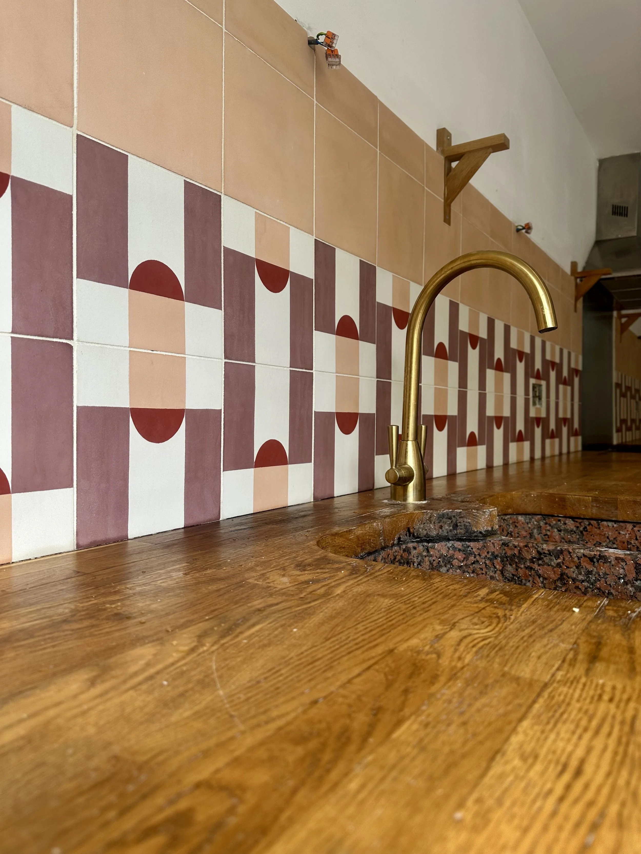 A kitchen countertop with a brass faucet, a wooden surface, a tiled backsplash, and a wall shelf with brackets.