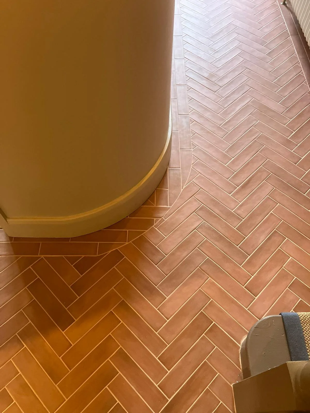 Close-up of a corner of a room with terracotta herringbone tile flooring and beige rounded wall.